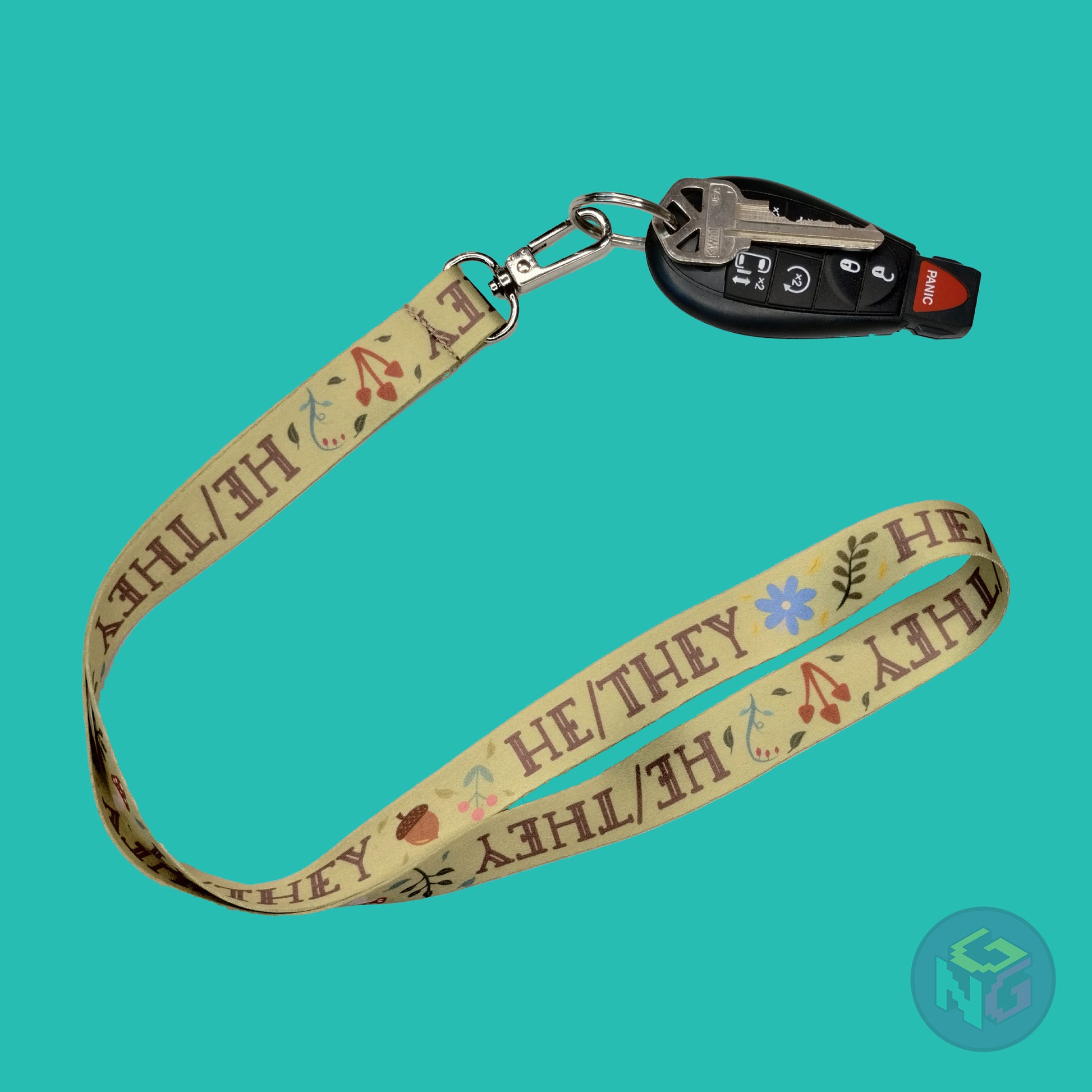 green he they pronoun lanyard showing the brown text, mushrooms, leaves, and flower details with a key fob clipped to the end of the lanyard