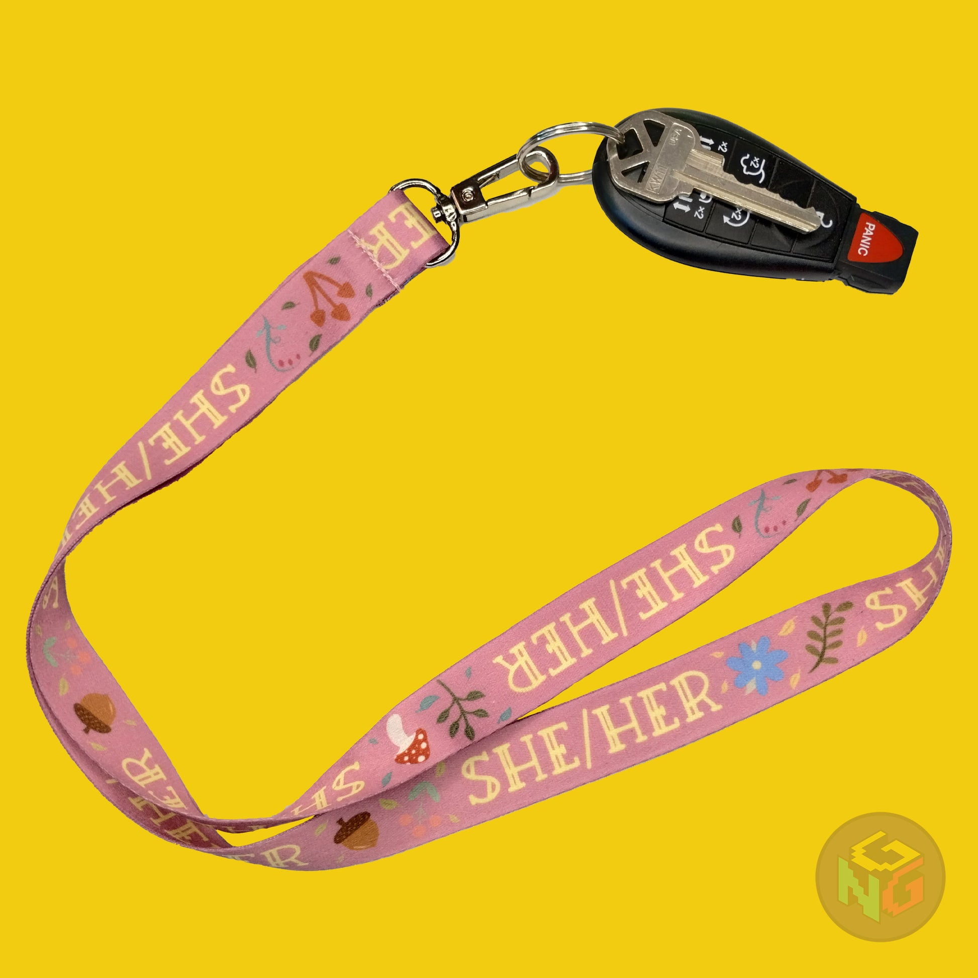 pink she her pronoun lanyard showing the yellow text, mushrooms, leaves, and flower details with a key fob clipped to the end of the lanyard