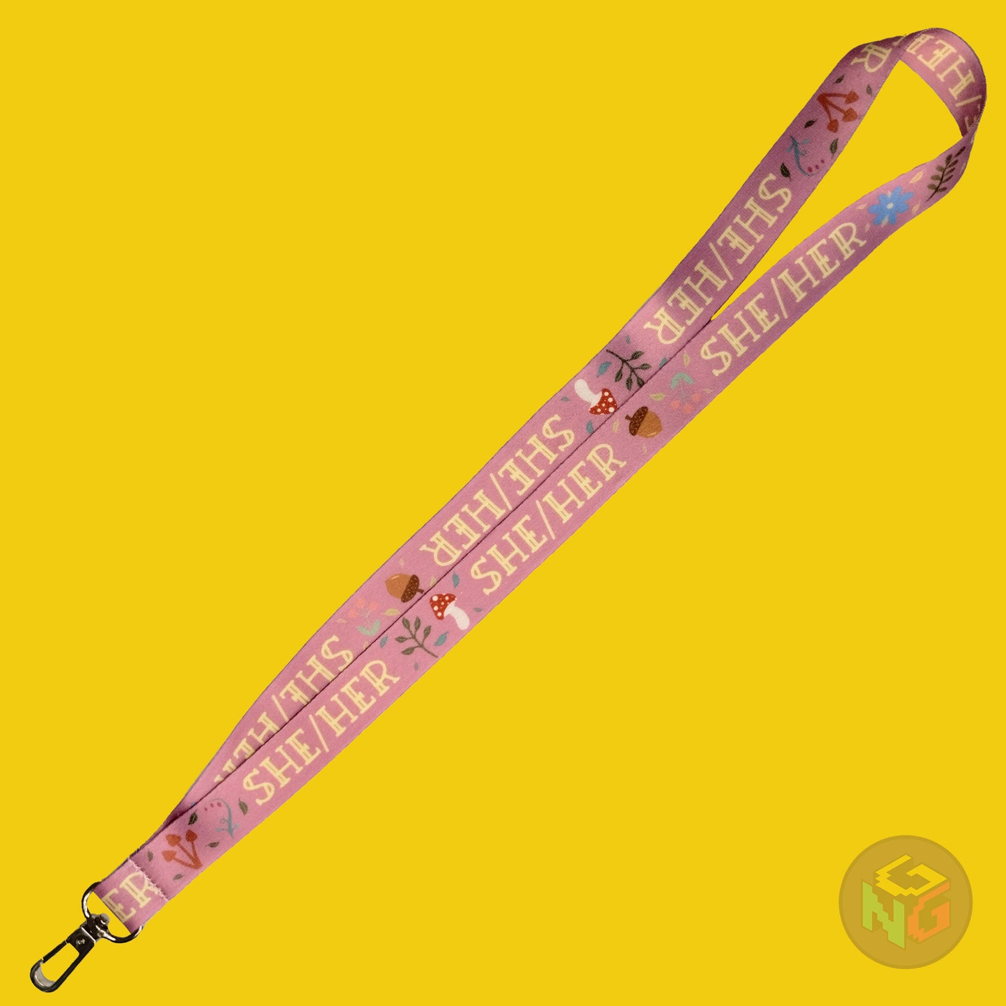 the pink she her cottagecore lanyard lying flat showing the complete design and repeating pattern of acorns, berries, mushrooms, leaves, and she her pronouns