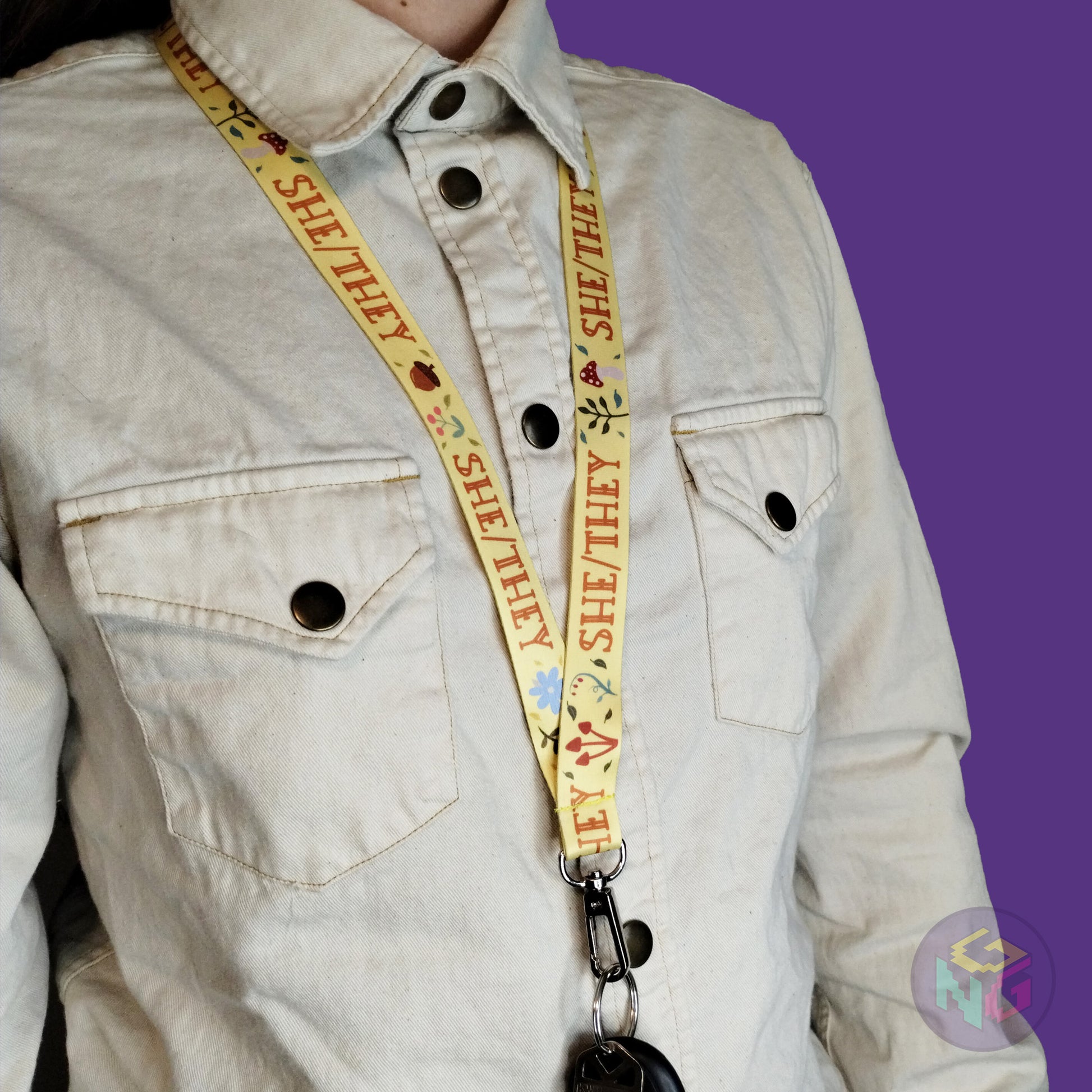 yellow she they mushroom lanyard being worn by a flat chested person wearing a cream button up. The end of the lanyard falls between their sternum and bellybutton and has a key fob clipped to the end