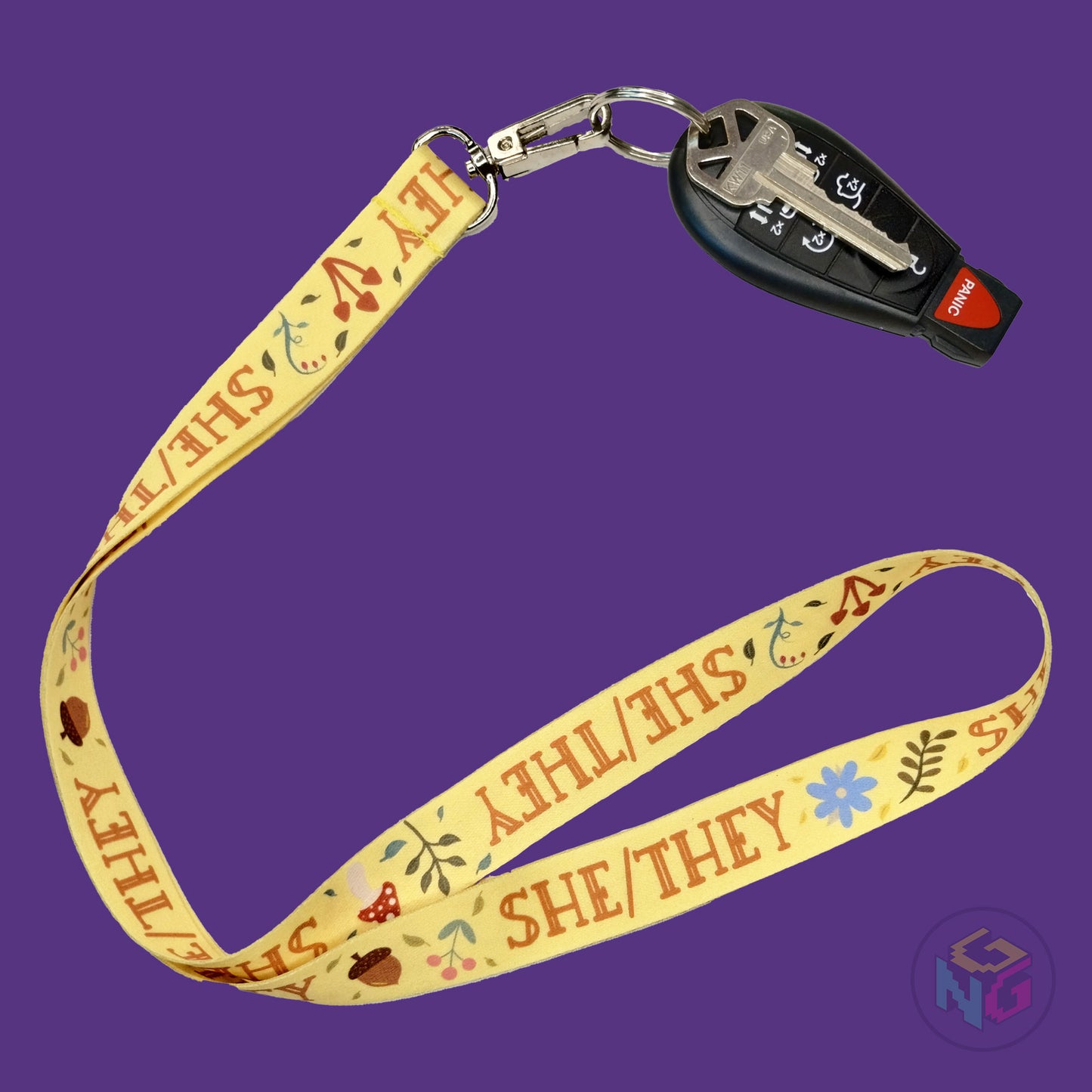 yellow she they pronoun lanyard showing the brown text, mushrooms, leaves, and flower details with a key fob clipped to the end of the lanyard
