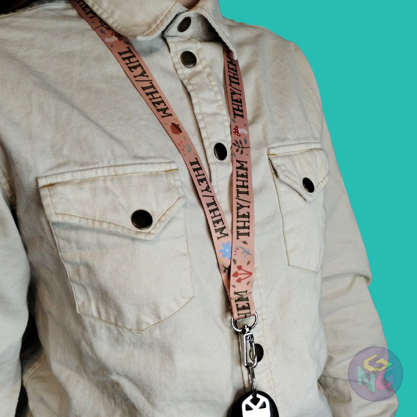 tan they them mushroom lanyard being worn by a flat chested person wearing a cream button up. The end of the lanyard falls between their sternum and bellybutton and has a key fob clipped to the end