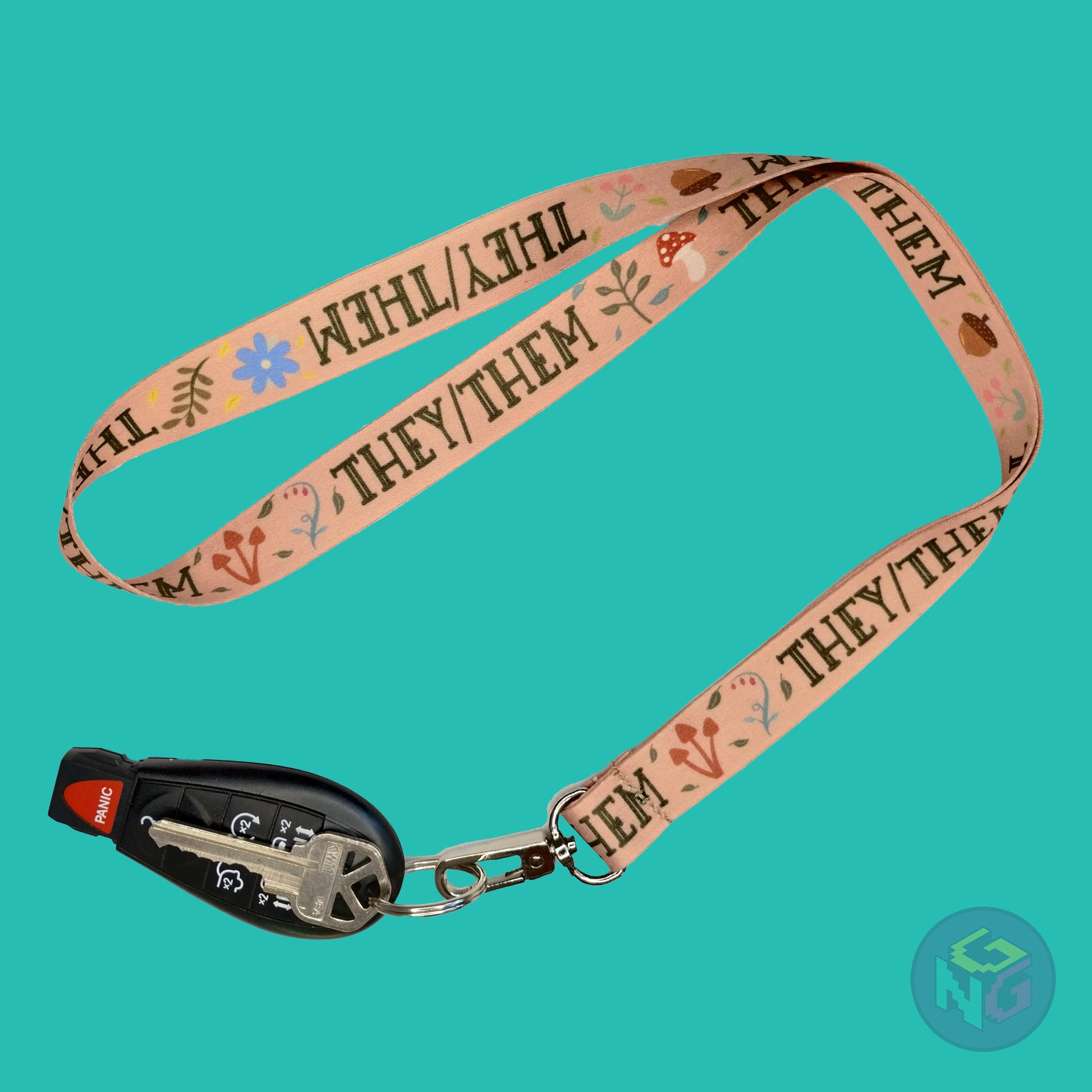 tan they them pronoun lanyard showing the green text, mushrooms, leaves, and flower details with a key fob clipped to the end of the lanyard