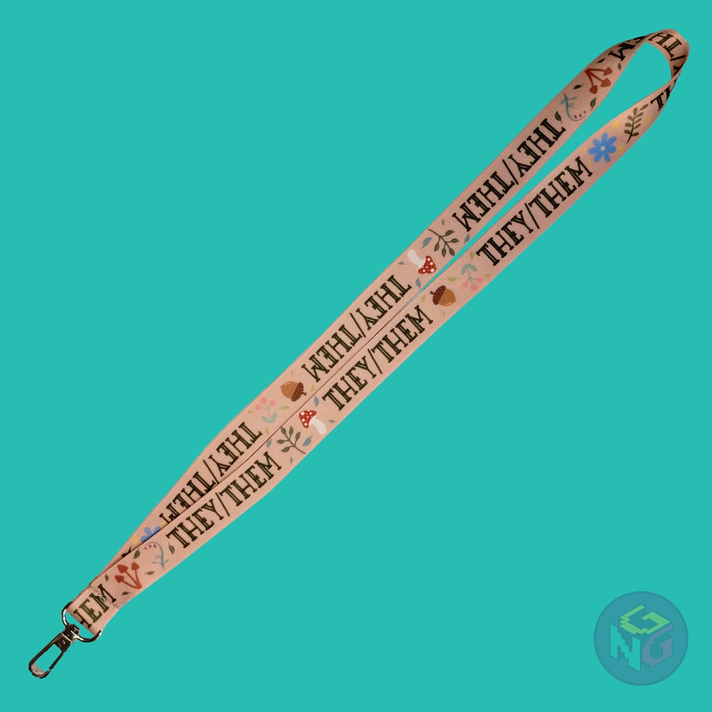 the tan they them cottagecore lanyard lying flat showing the complete design and repeating pattern of acorns, berries, mushrooms, leaves, and they them pronouns