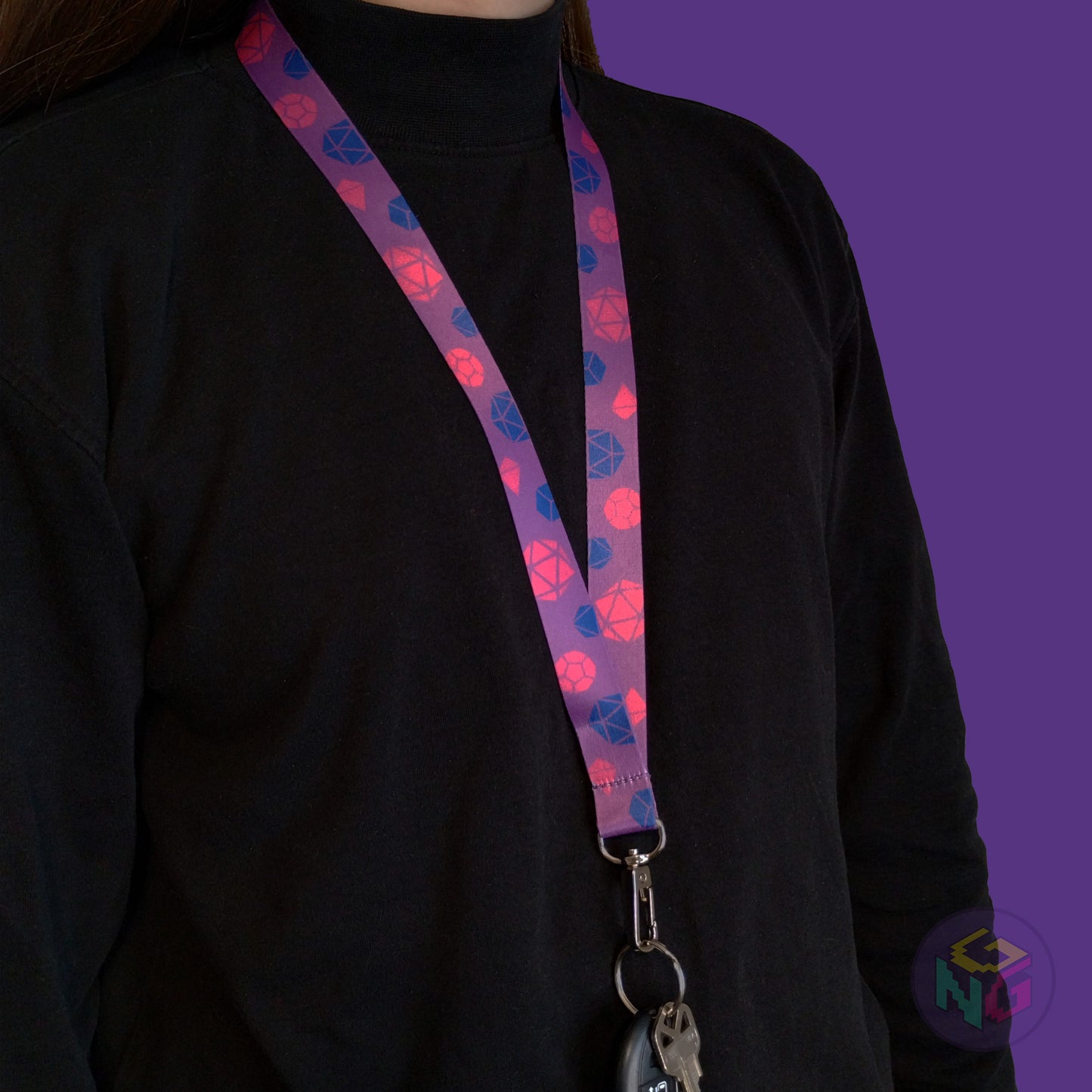 purple bisexual pride lanyard being worn by a flat chested person wearing a black turtleneck. The end of the lanyard falls between their sternum and bellybutton and has a key fob clipped to the end