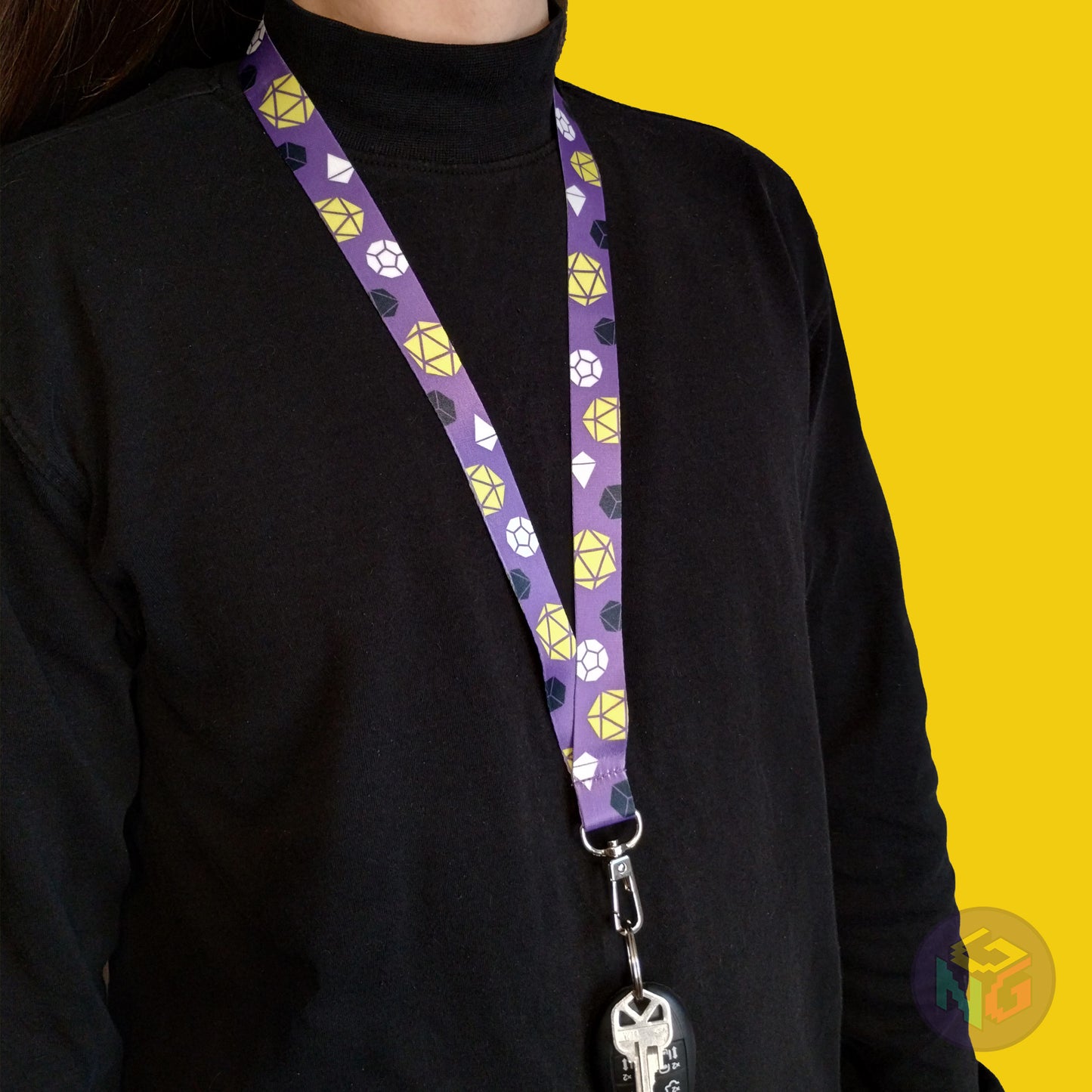 purple nonbinary pride lanyard being worn by a flat chested person wearing a black turtleneck. The end of the lanyard falls between their sternum and bellybutton and has a key fob clipped to the end