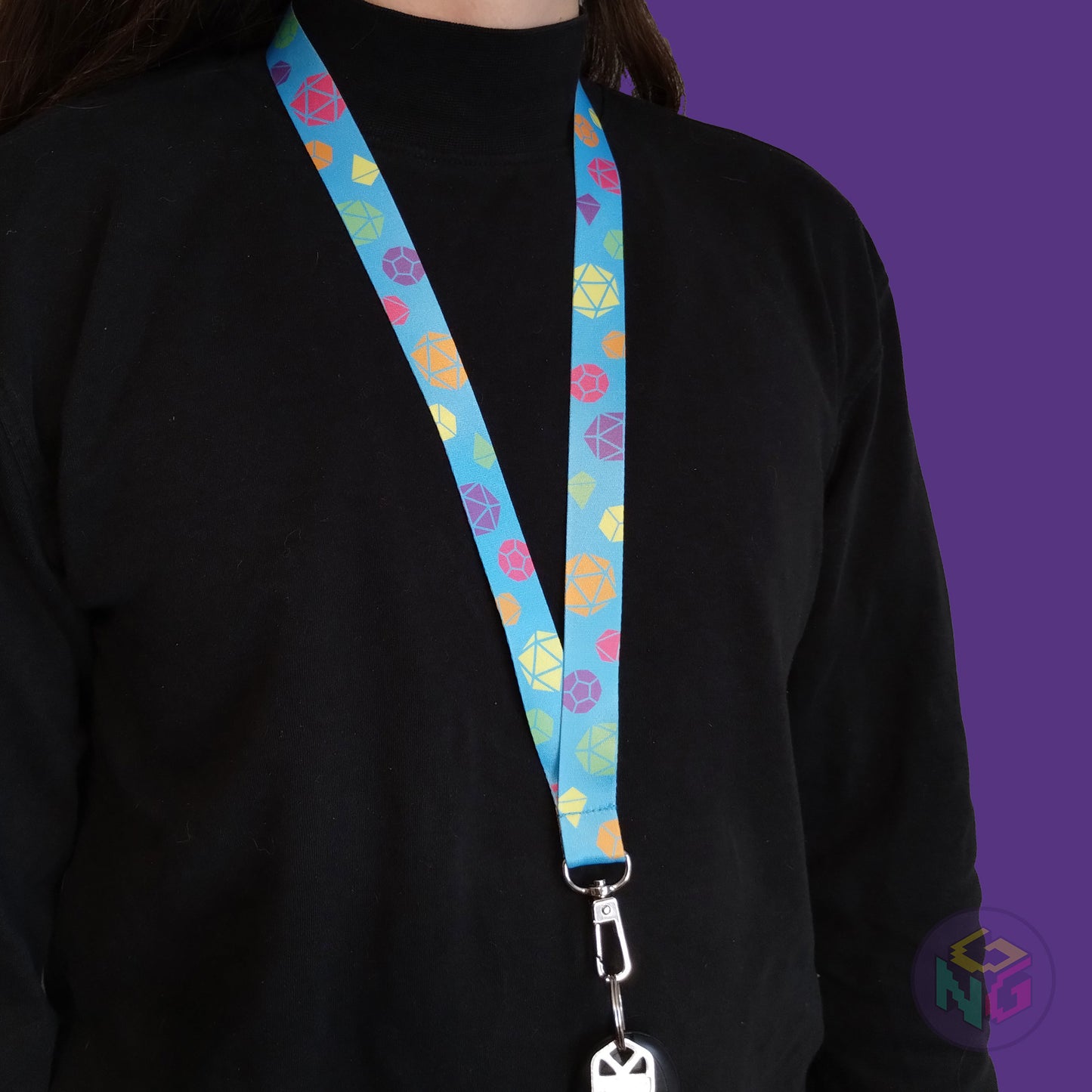 blue rainbow pride lanyard being worn by a flat chested person wearing a black turtleneck. The end of the lanyard falls between their sternum and bellybutton and has a key fob clipped to the end