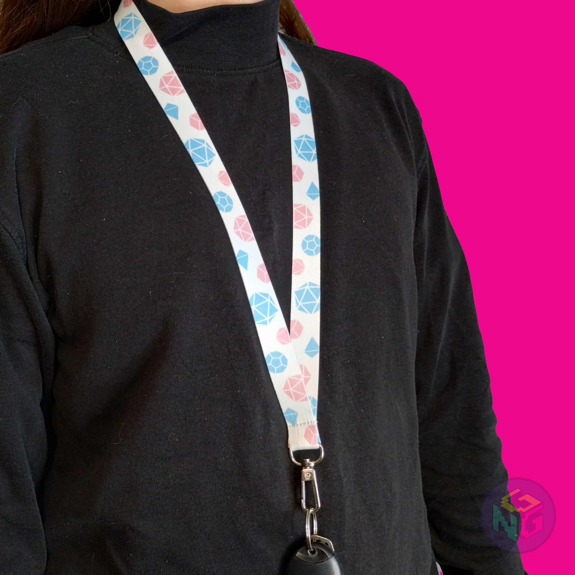white transgender pride lanyard being worn by a flat chested person wearing a black turtleneck. The end of the lanyard falls between their sternum and bellybutton and has a key fob clipped to the end