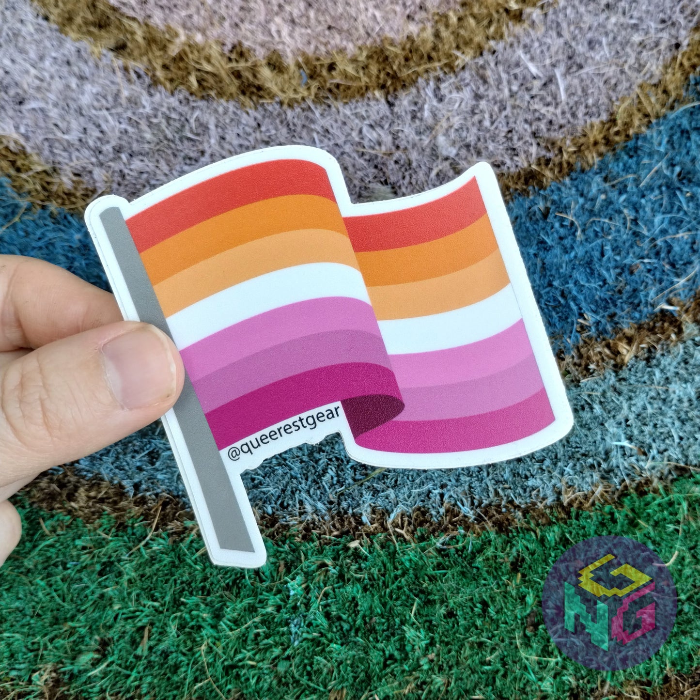 lesbian flag sticker being held in front of rainbow welcome mat