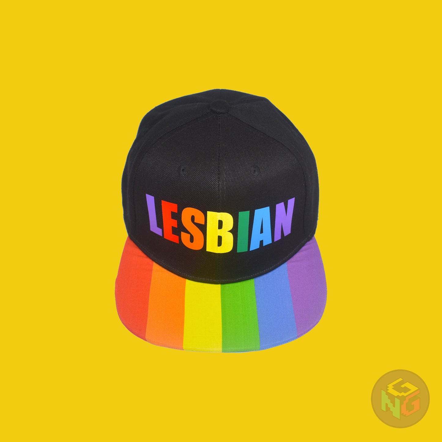 Black flat bill snapback hat. The brim has the rainbow pride flag on both sides and the front of the hat has the word “LESBIAN” in rainbow letters. Front top view