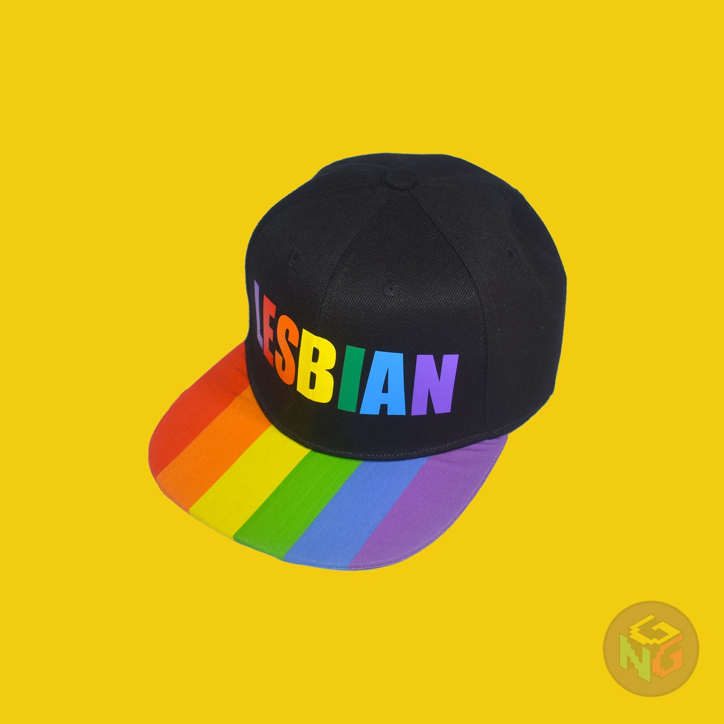 Black flat bill snapback hat. The brim has the rainbow pride flag on both sides and the front of the hat has the word “LESBIAN” in rainbow letters. Front left view