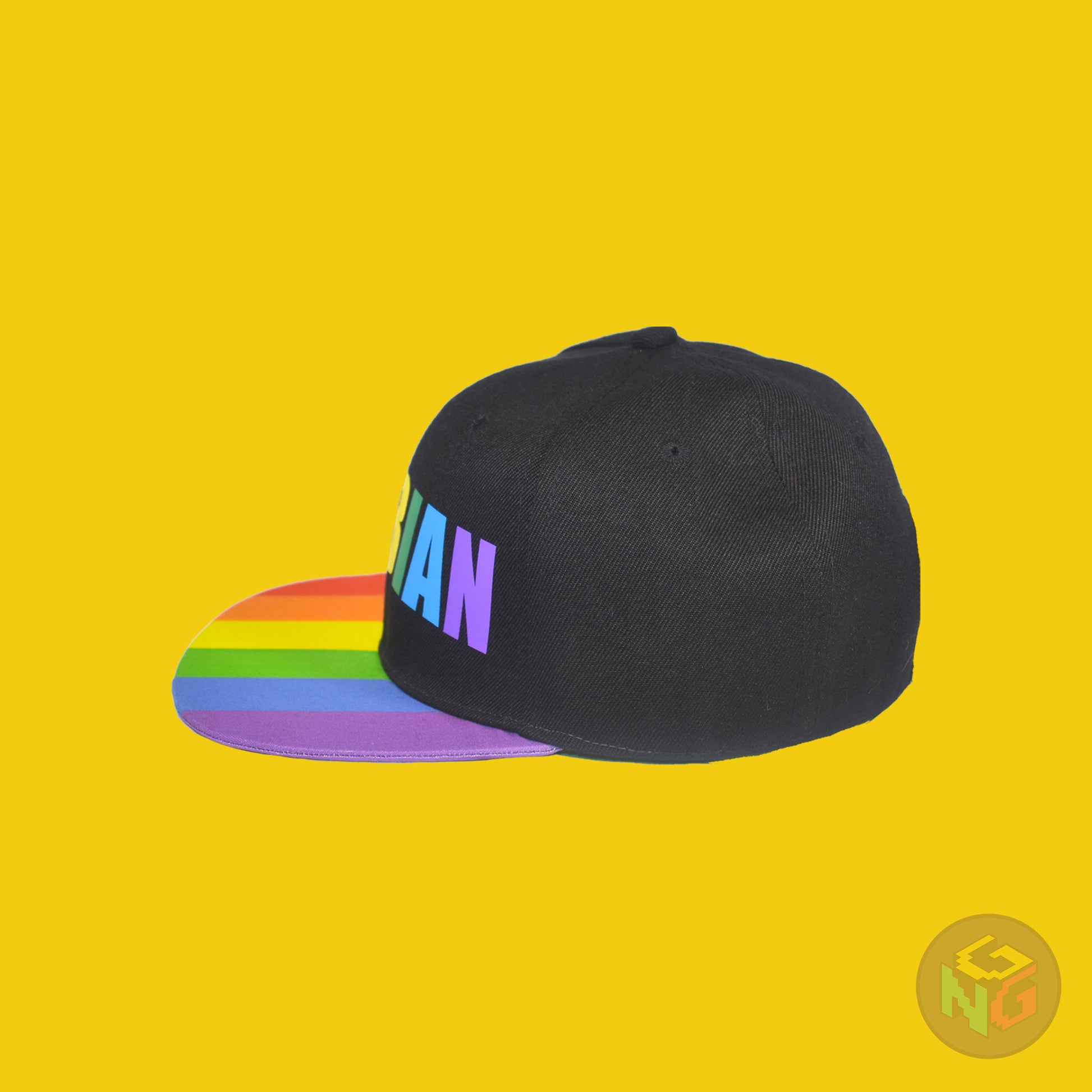 Black flat bill snapback hat. The brim has the rainbow pride flag on both sides and the front of the hat has the word “LESBIAN” in rainbow letters. Left view