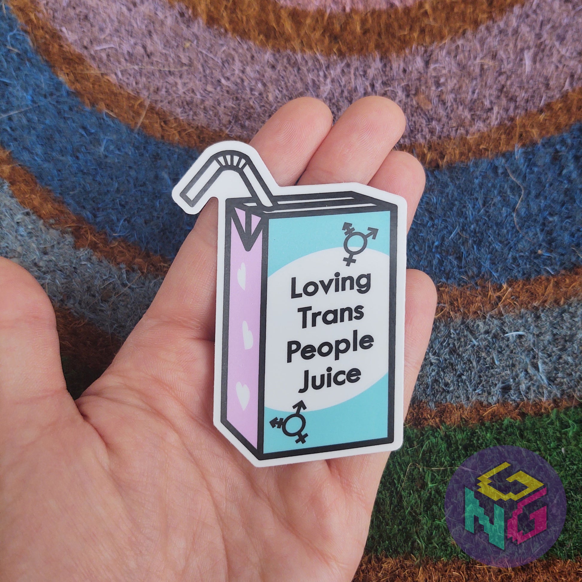 loving trans people juice sticker being held in hand in front of rainbow welcome mat