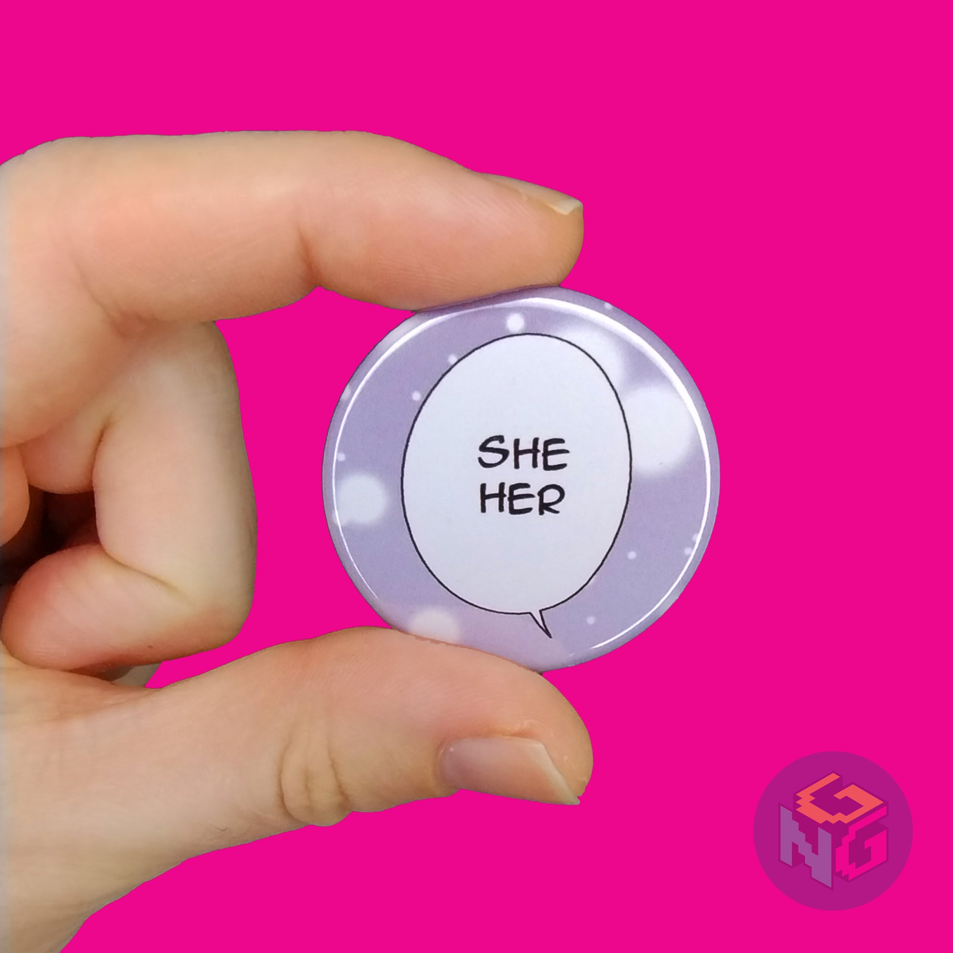 hand holding black and white she her comic pronoun pin in front of pink background
