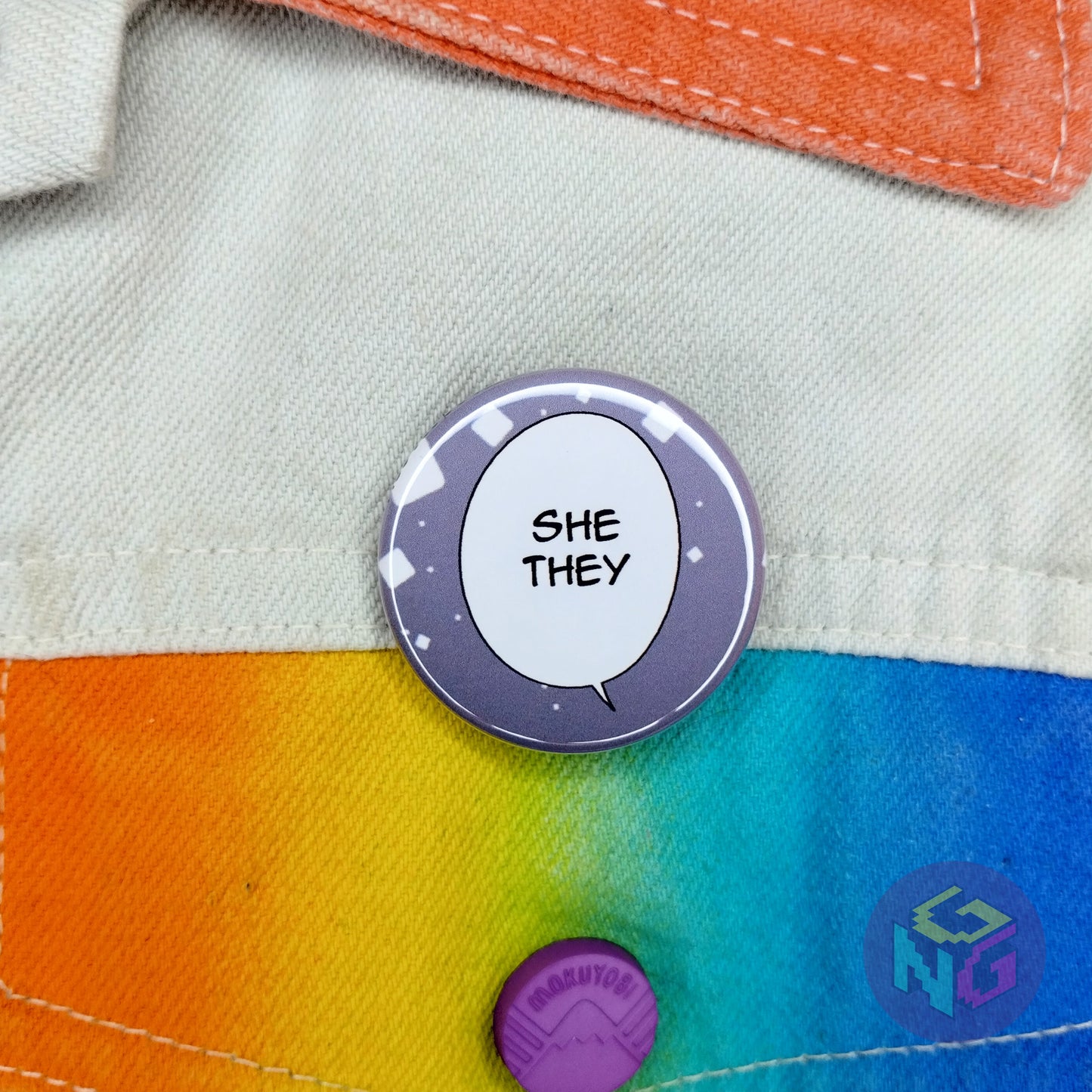 round she they comic panel pronoun button pinned to a white denim jacket with rainbow details