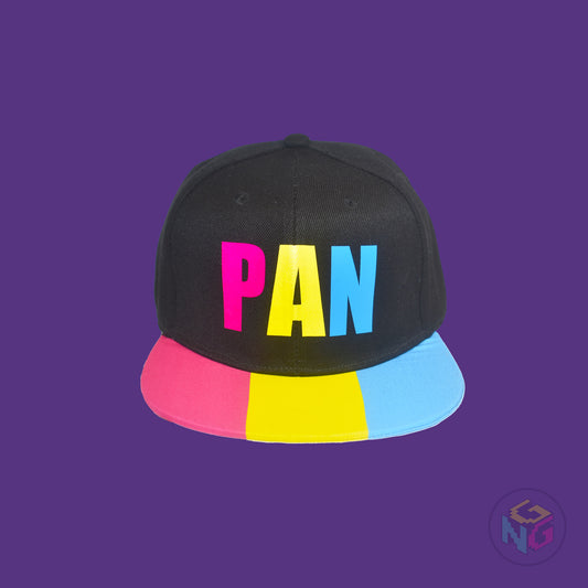 Black flat bill snapback hat. The brim has the pansexual pride flag on both sides and the front of the hat has the word “PAN” in pink, yellow, and blue letters. Front view