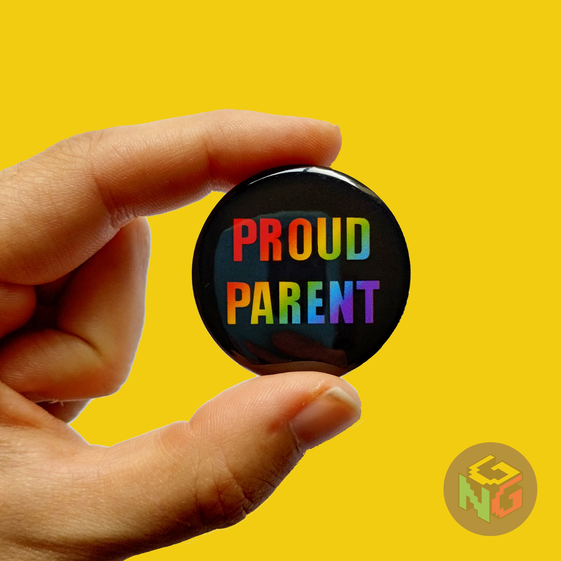 black and rainbow proud parent pin held in a hand in front of a yellow background