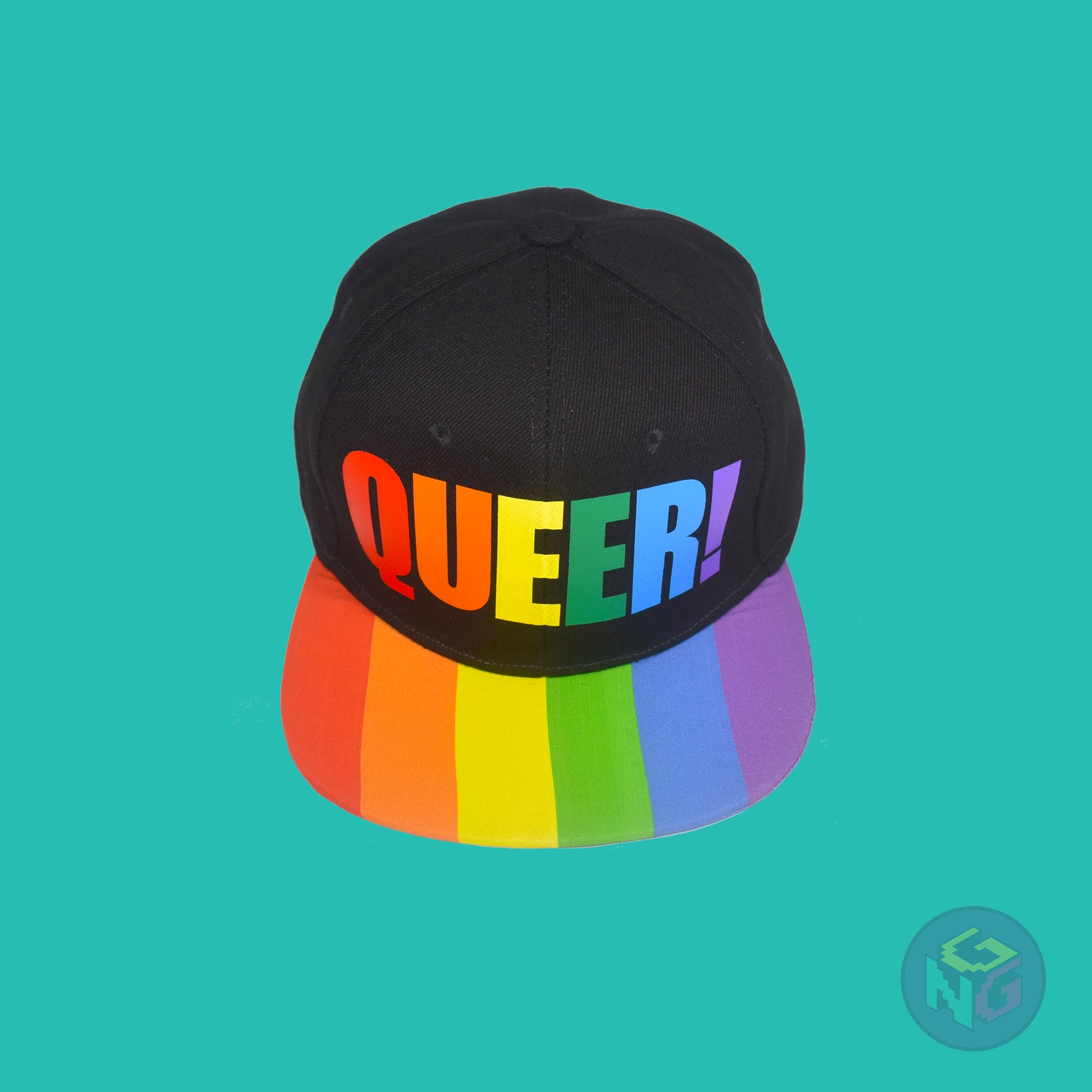Black flat bill snapback hat. The brim has the rainbow pride flag on both sides and the front of the hat has the word “QUEER!” in rainbow letters. Front top view