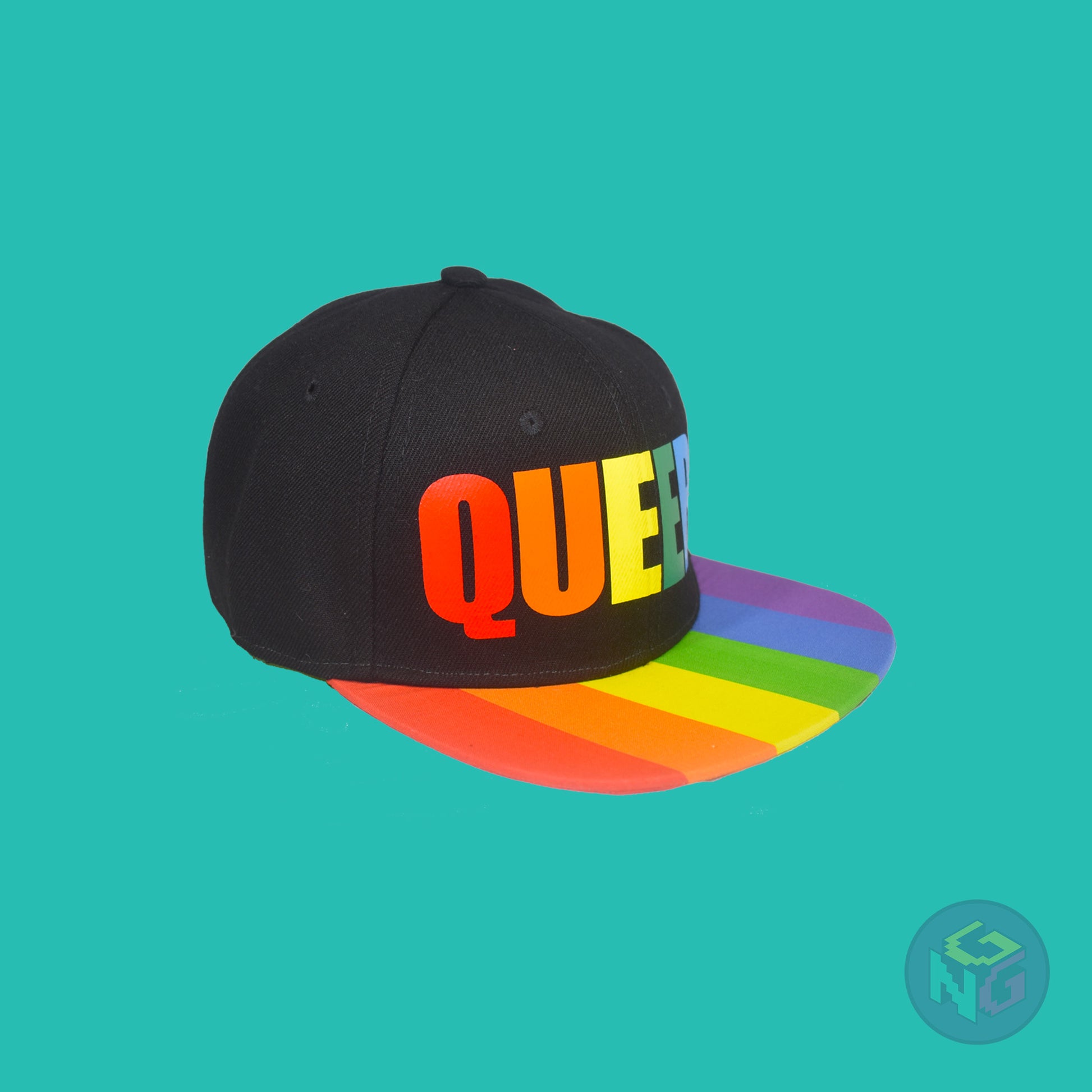 Black flat bill snapback hat. The brim has the rainbow pride flag on both sides and the front of the hat has the word “QUEER!” in rainbow letters. Front right view