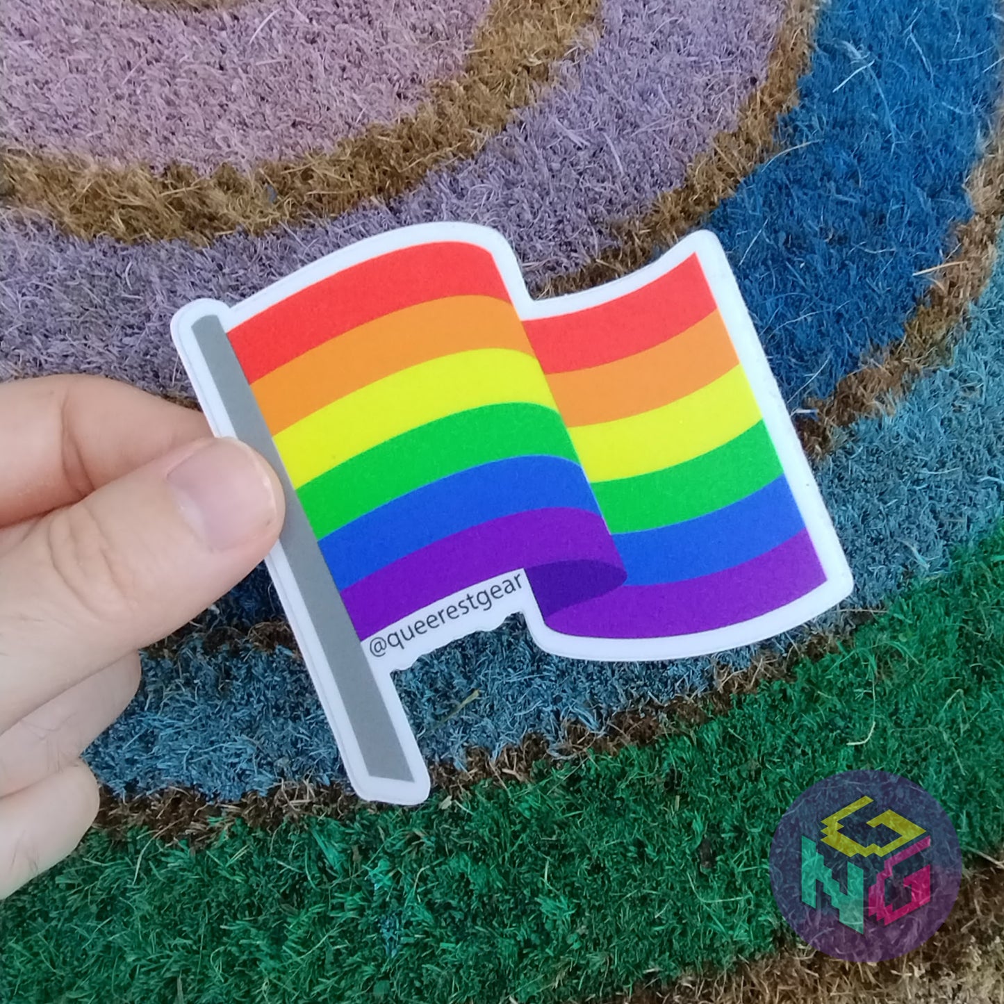 rainbow flag sticker held in front of a rainbow welcome mat