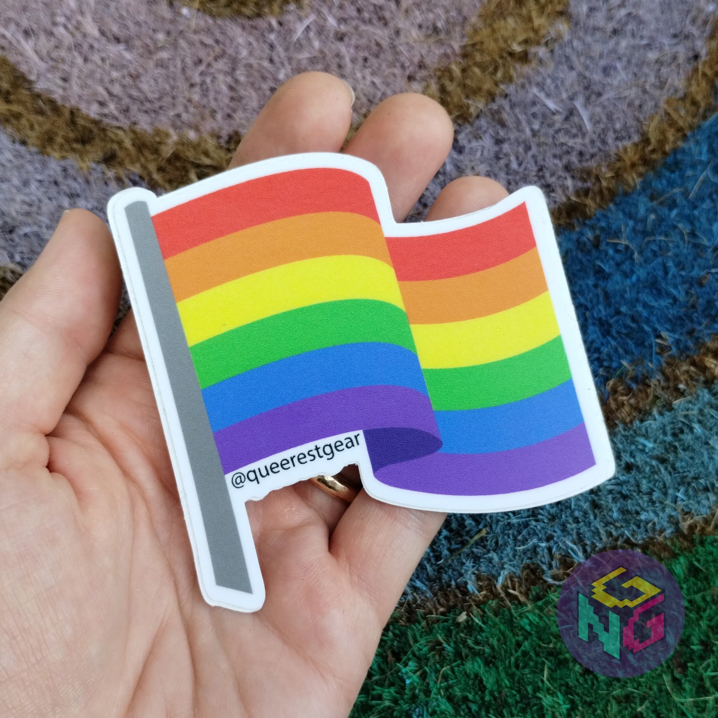 rainbow flag sticker held in a hand on a background of a rainbow welcome mat