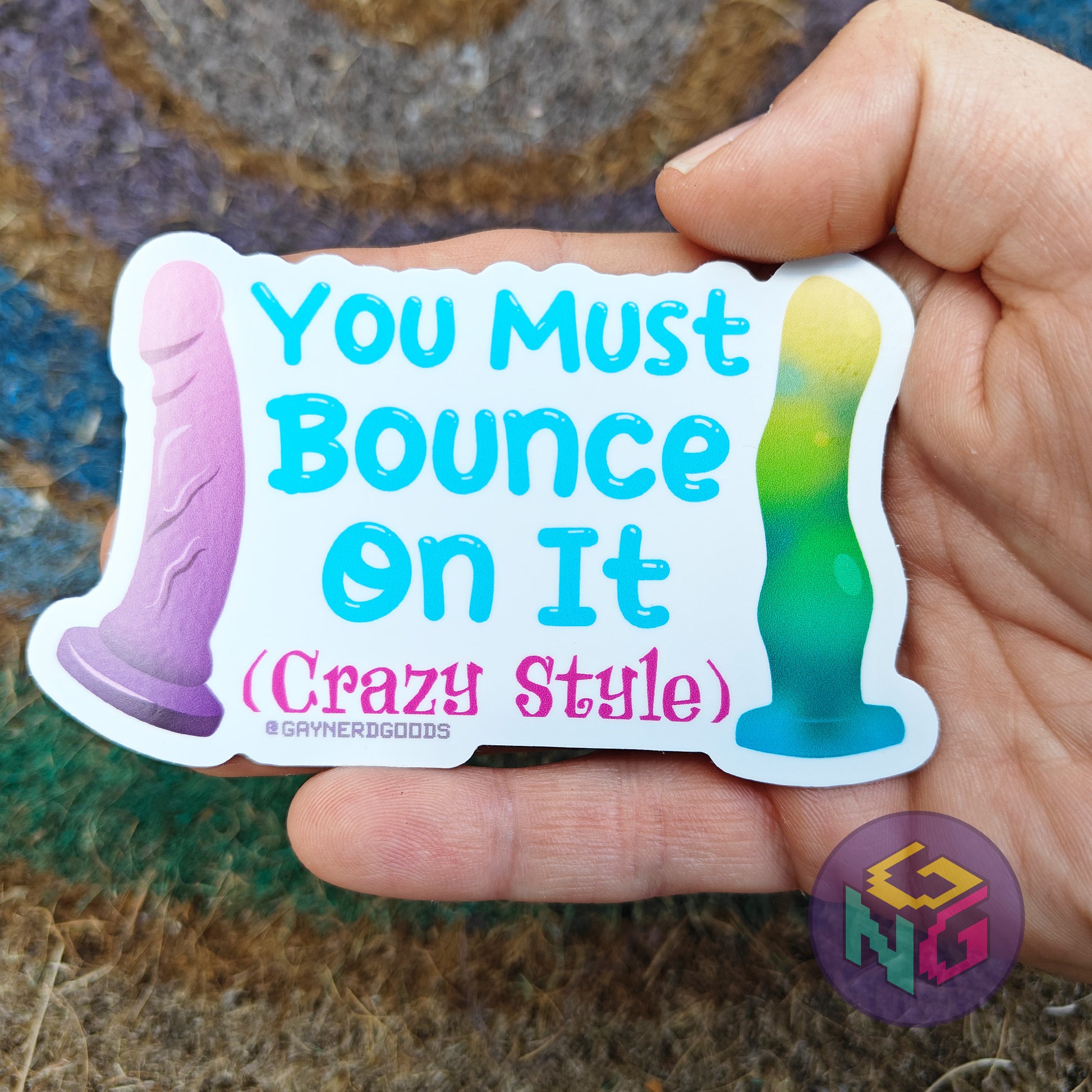 Hand holding a colorful sticker with text 'You Must Bounce On It (Crazy Style)' against a textured background.