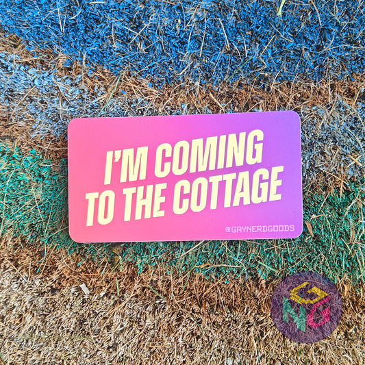 A rectangular pink and purple gradient sticker with yellow text that reads "I'm coming to the cottage". The sticker is lying flat on a rough rainbow background