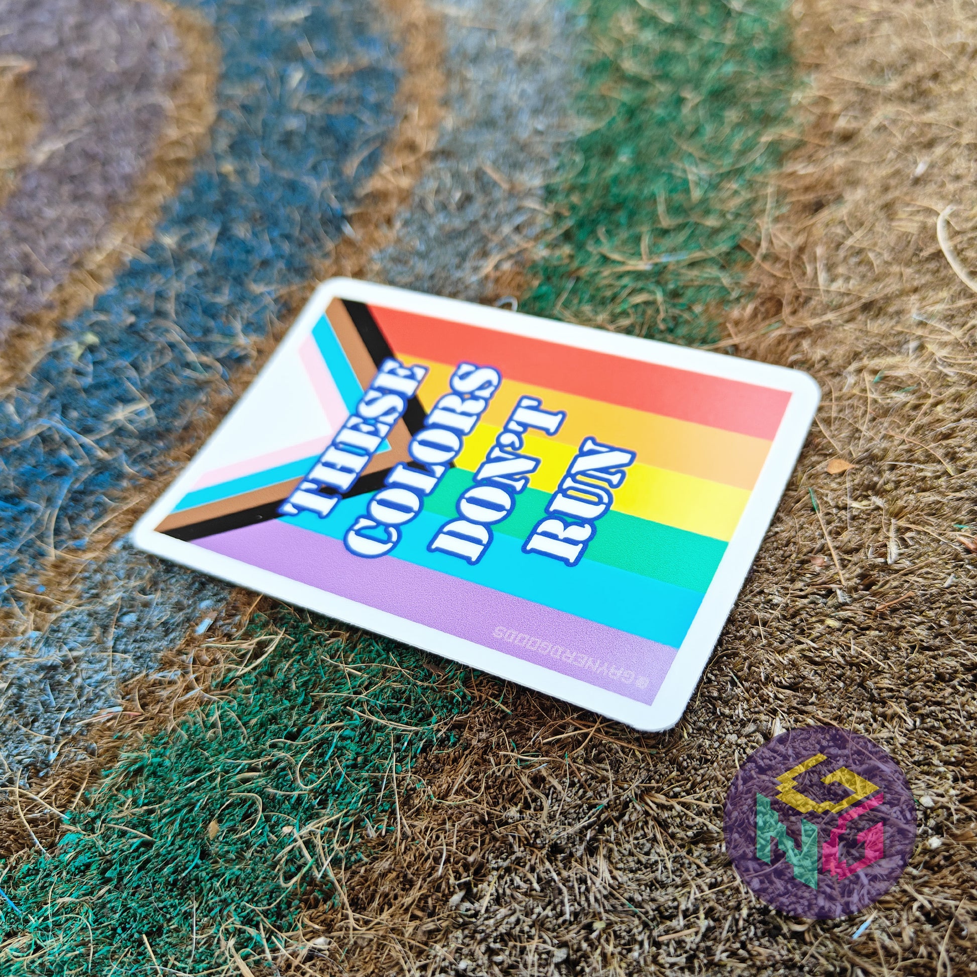Colorful gay pride sticker with 'These colors don't run' text at an angle on a textured surface