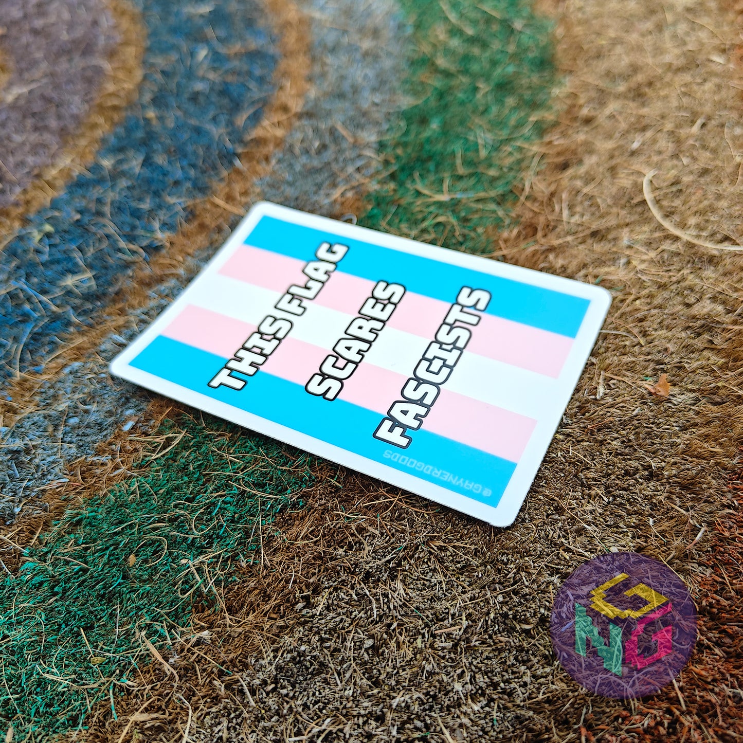 trans pride flag vinyl sticker with bold white text "this flag scares fascists" laying at an angle