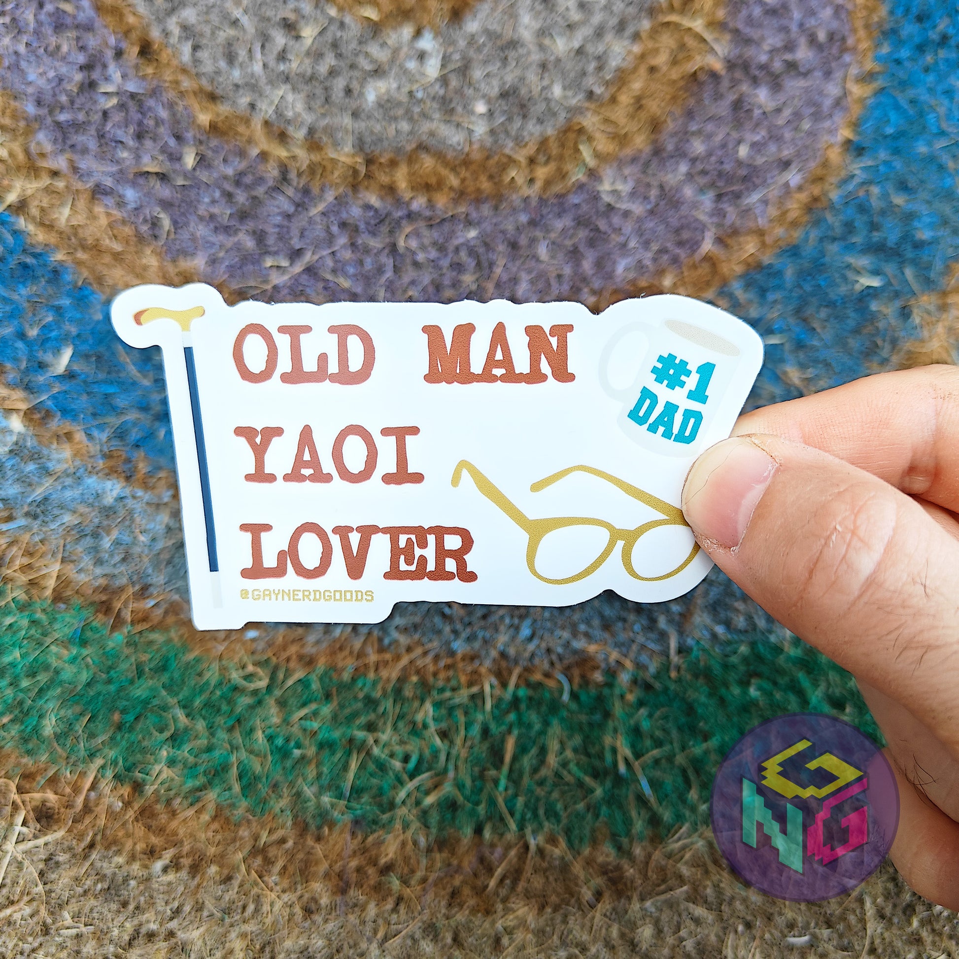gay pride sticker with text 'OLD MAN YAOI LOVER' held over a textured surface