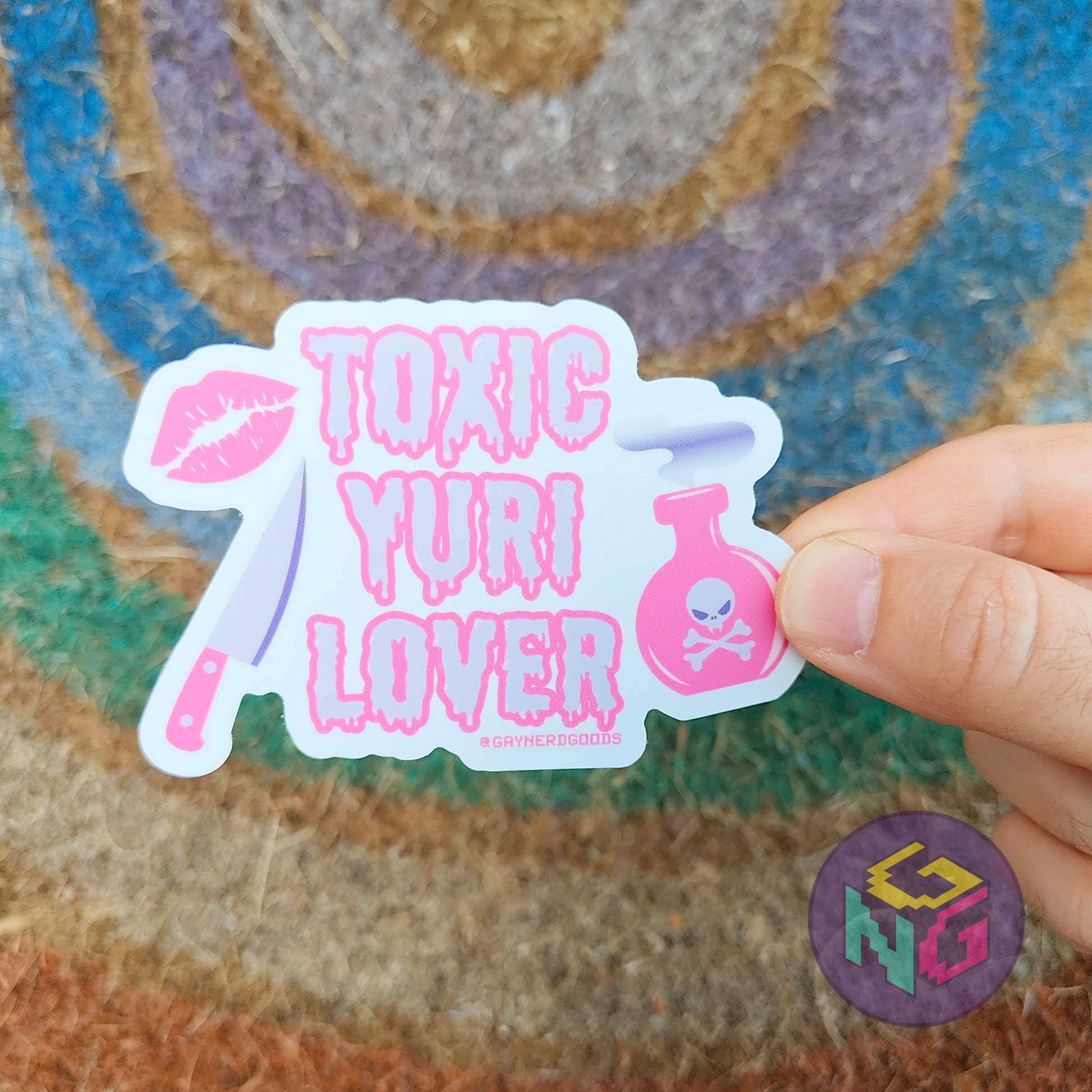 lesbian pride sticker with 'Toxic Yuri Lover' text held by a hand against a textured background