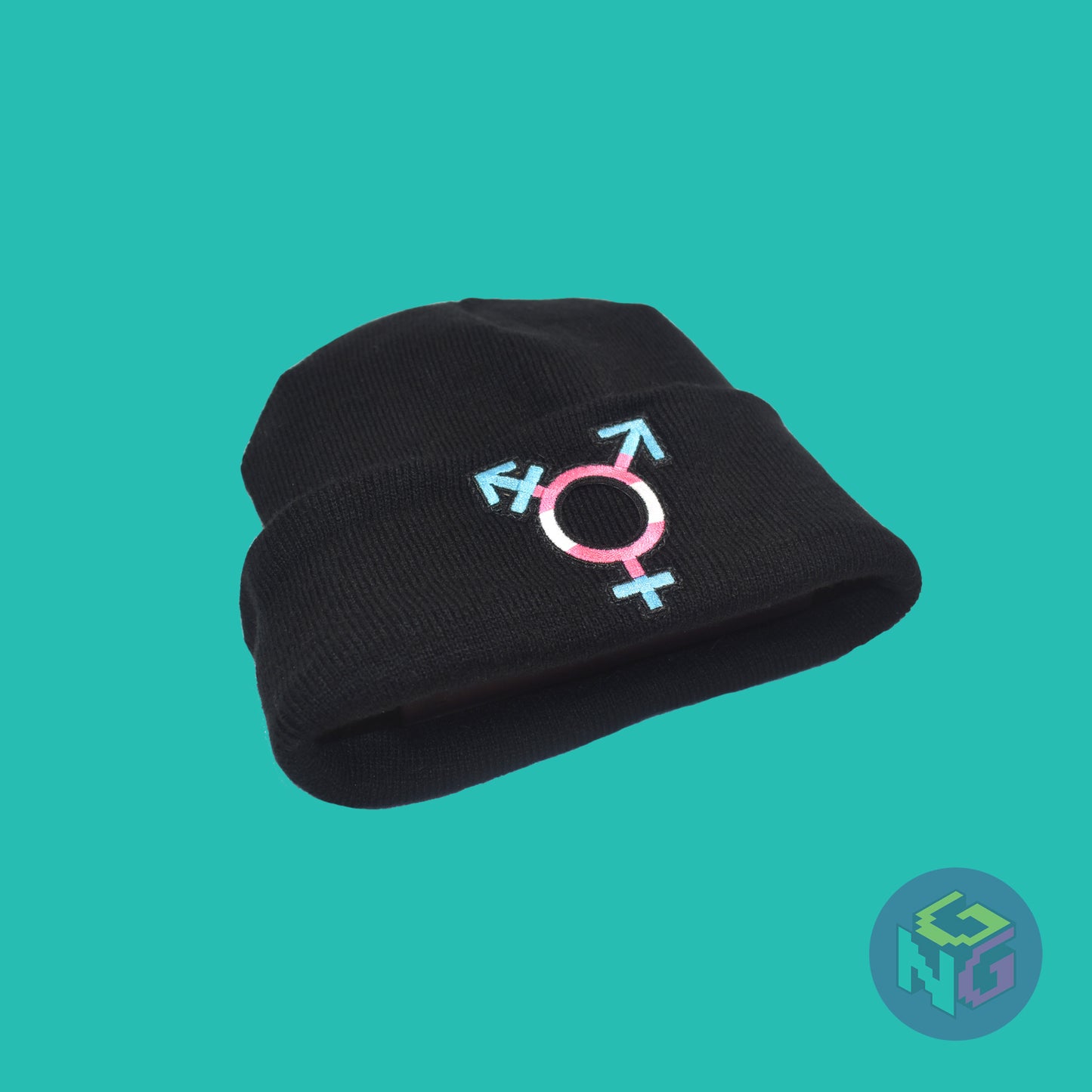 Black knit fabric beanie with the transgender symbol in blue, pink, and white on the front. It is laying flat, seen from the lower left on a mint green background