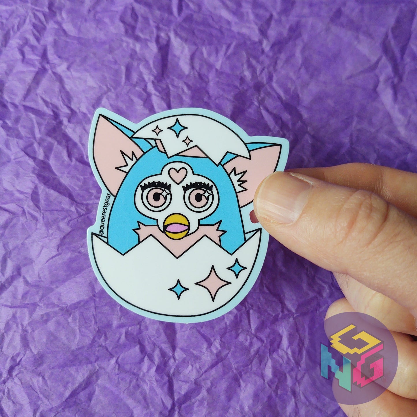 transgender furby sticker breaking out of an egg held in front of a purple background