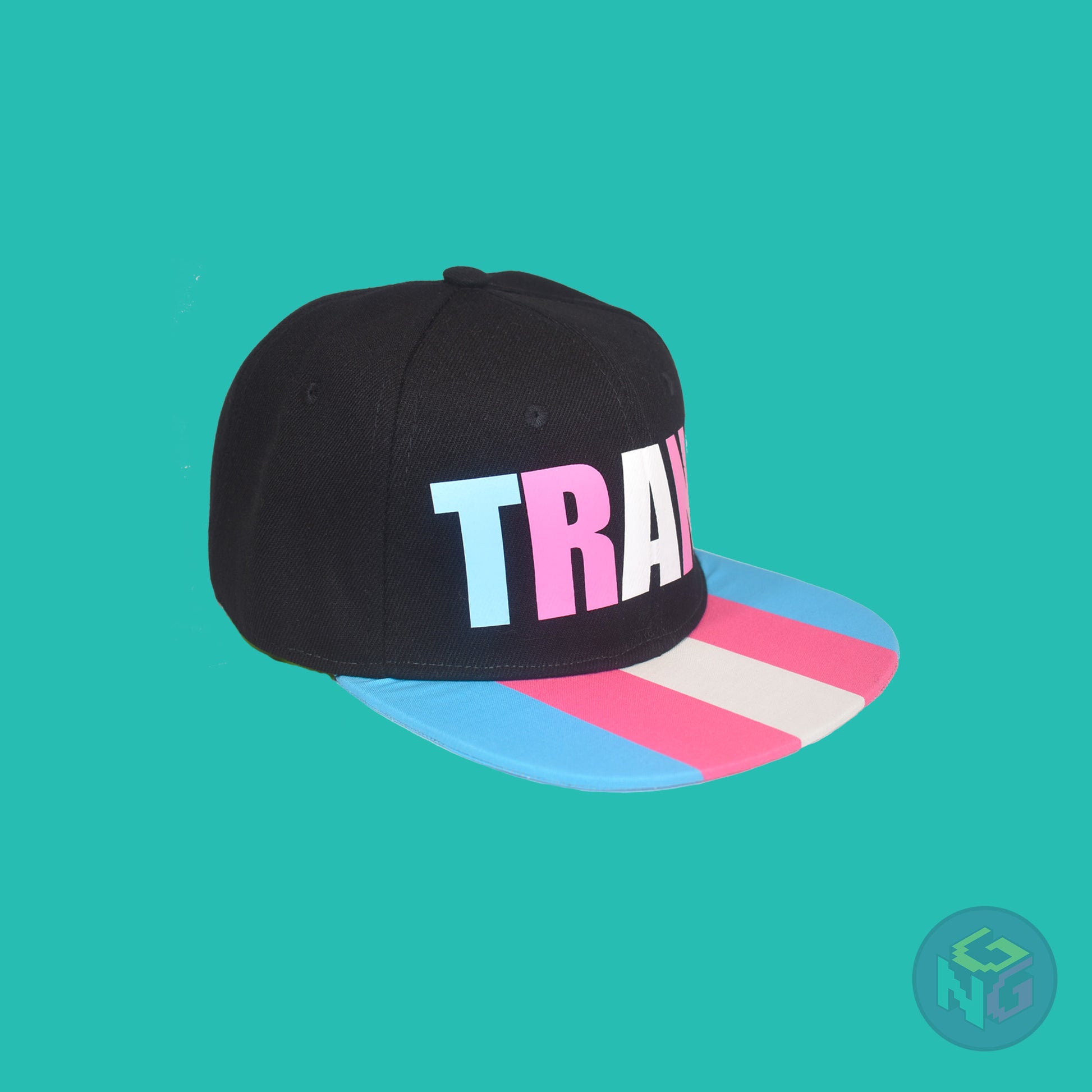 Black flat bill snapback hat. The brim has the transgender pride flag on both sides and the front of the hat has the word “TRANS” in blue, pink, and white letters. Front right view