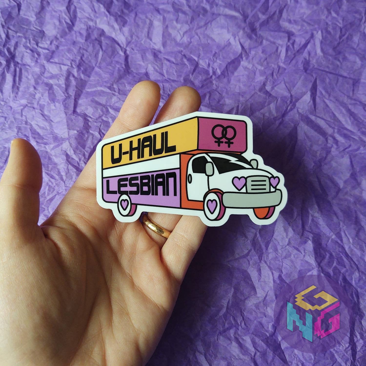 u-haul lesbian sticker held in a hand in front of purple background