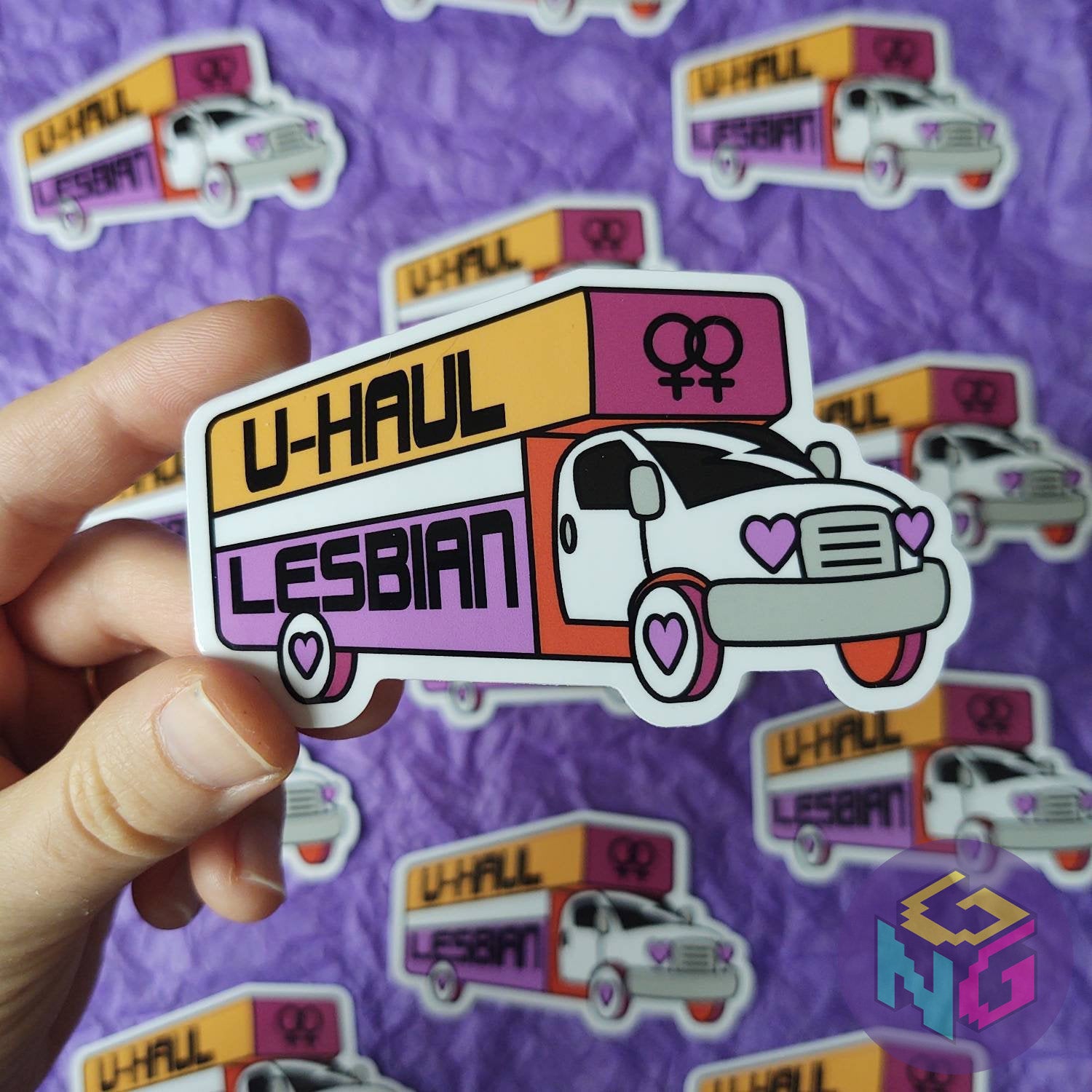 hand holding uhaul lesbian sticker in front of more u-haul lesbian stickers on purple background