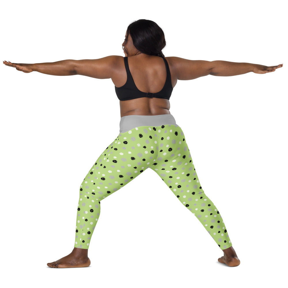 back view of dark-skinned female-presenting plus size model wearing the agender dnd dice leggings and a black sports bra. She is doing a warrior yoga pose with arms extended