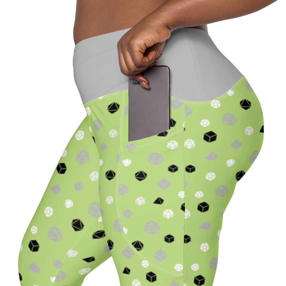 left side view of the agender dnd dice plus size leggings. the dark-skinned female-presenting model is sliding her phone into one of the side pockets