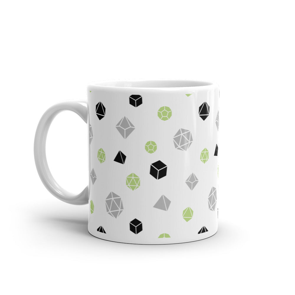 white mug on a white background with handle facing left. It has an all-over print of polyhedral d&d dice in the agender colors of green, grey, and black