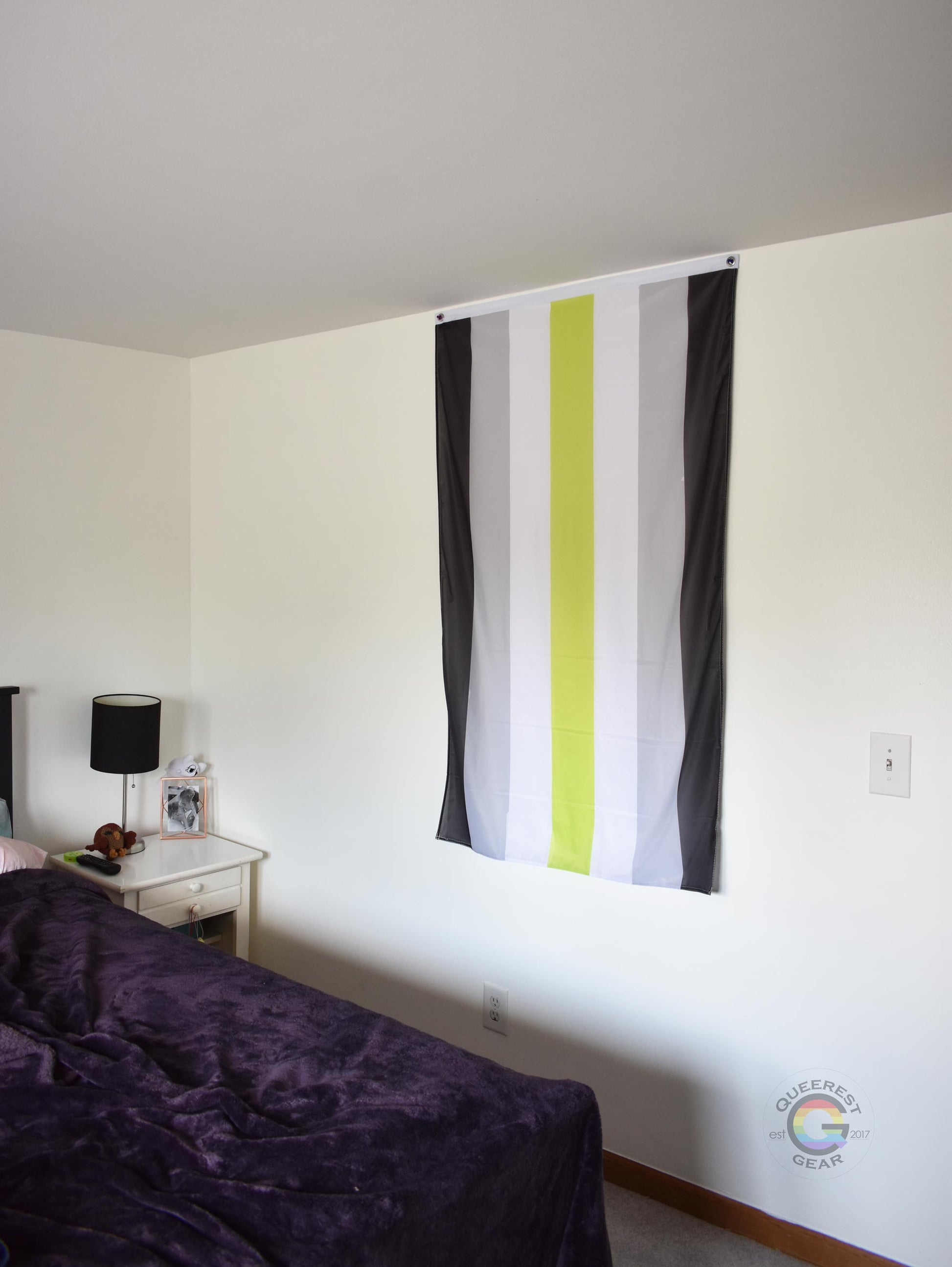 3’x5’ agender pride flag hanging vertically on the wall of a bedroom with a nightstand and a bed