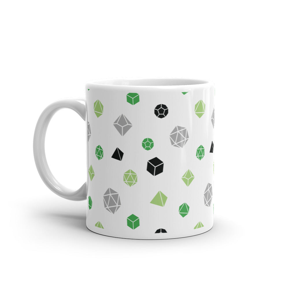 white mug on a white background with handle facing left. It has an all-over print of polyhedral d&d dice in the aromantic colors of greens, grey, and black