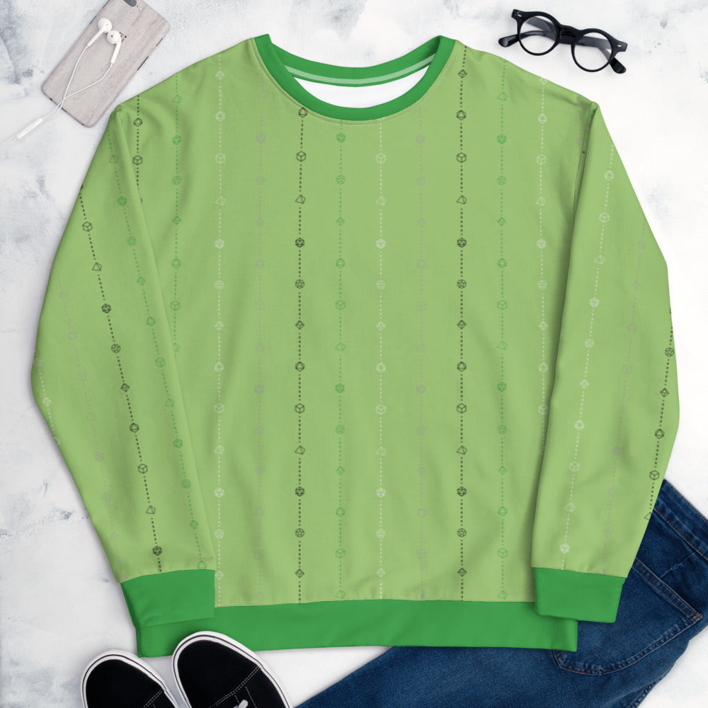 The aromantic pride sweater laying flat, surrounded by clothes, a phone, and glasses. the sweater is light green and has stripes of dashed lines and polyhedral dnd dice in green, grey, white, and black. The cuffs, collar, and waistband are green
