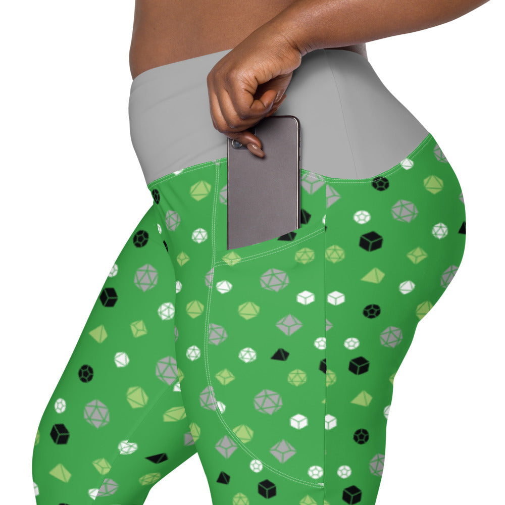 left side view of the aromantic dnd dice plus size leggings. the dark-skinned female-presenting model is sliding her phone into one of the side pockets