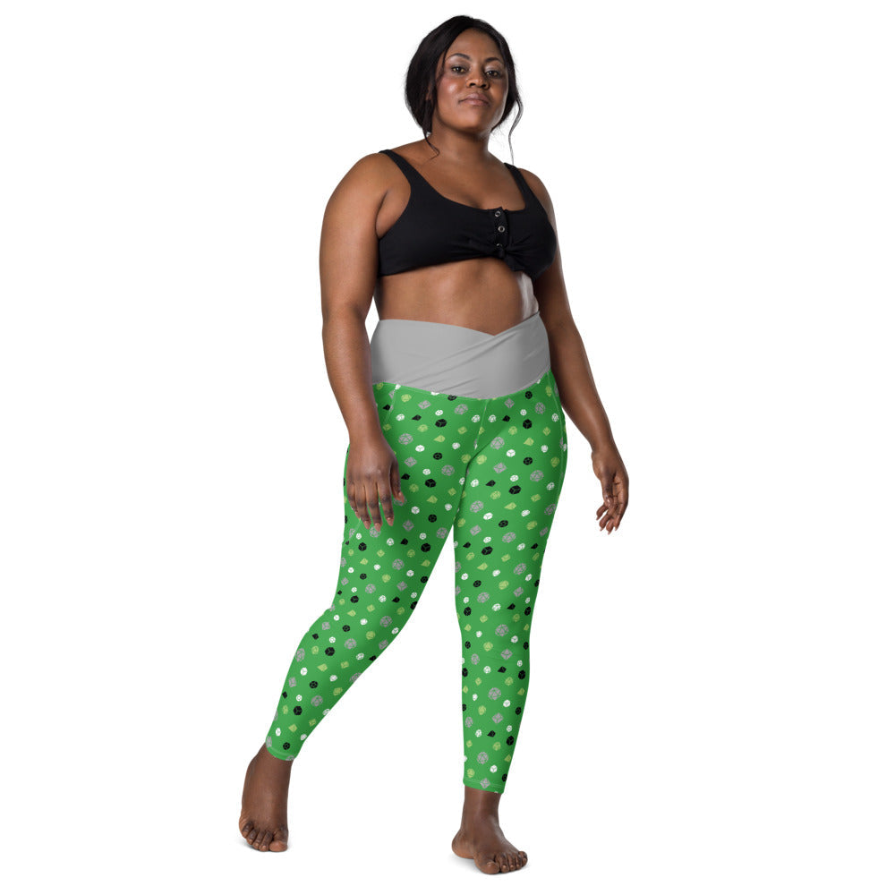 front view of dark-skinned female-presenting plus size model wearing the aromantic dice leggings and a black sports bra. This view shows off the grey crossover high-rise waistband