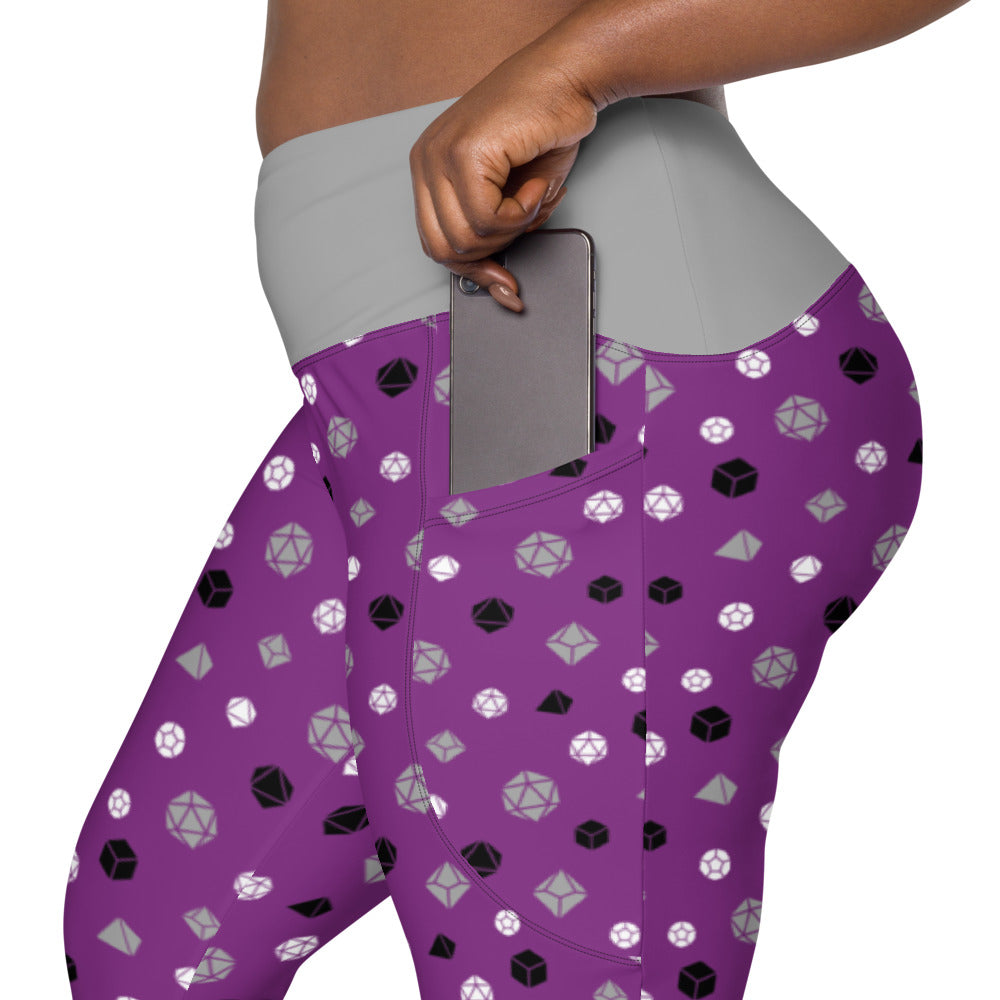 left side view of asexual dnd dice plus size leggings. the dark-skinned female-presenting model is sliding her phone into one of the side pockets