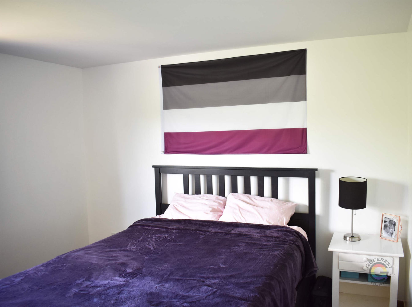 3’x5’ asexual pride flag hanging horizontally on the wall of a bedroom centered above a bed with a purple blanket