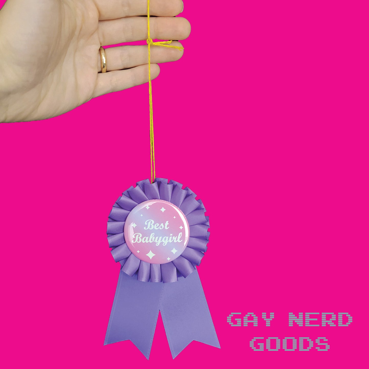 hand holding the best babygirl award ribbon by the thread loop on a hot pink background