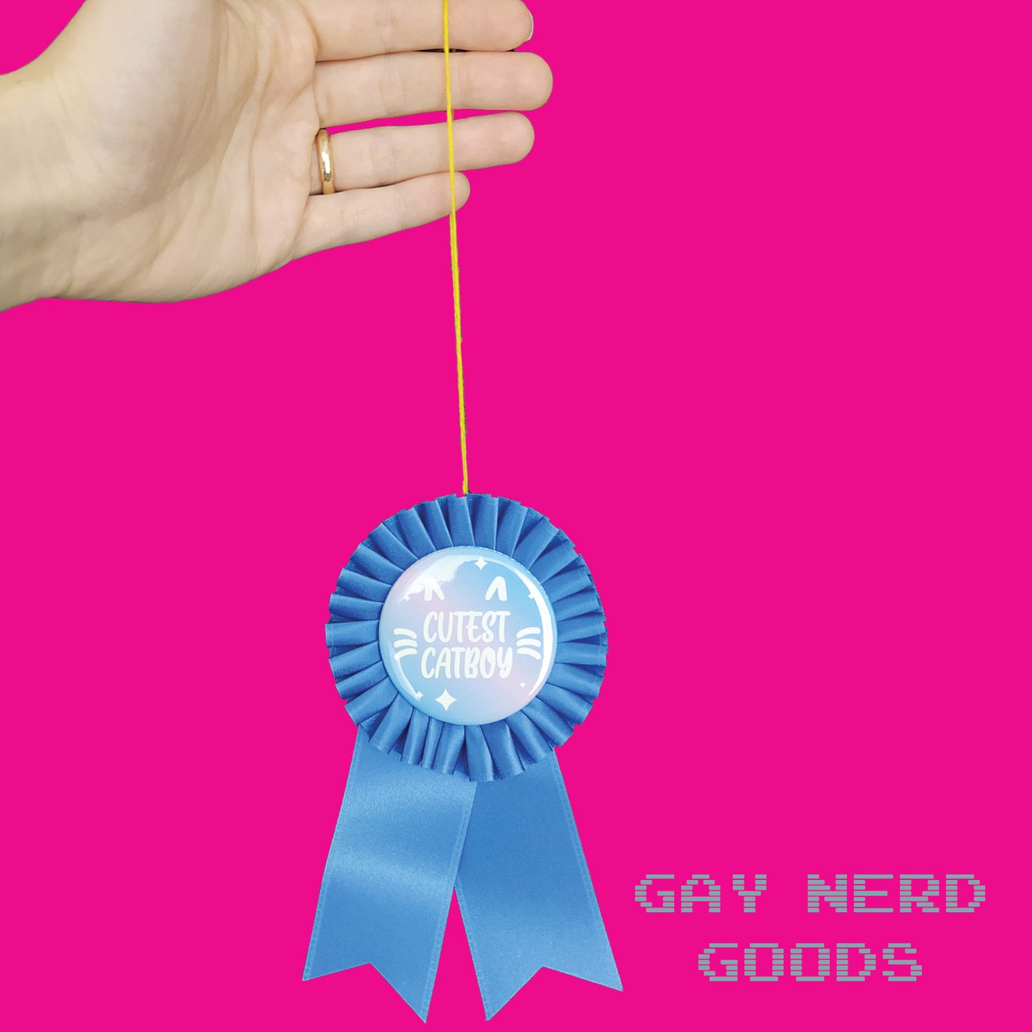 hand holding the blue "cutest catboy" award ribbon by its thread loop against a pink background