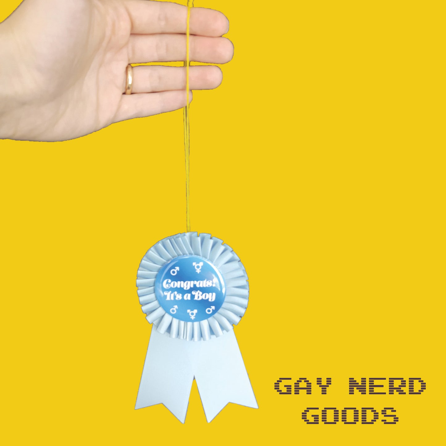hand holding the thread of the congrats it's a boy gender reveal ribbon on a yellow background
