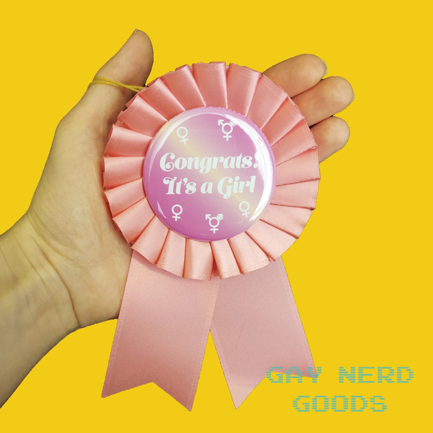 hand holding the "congrats! it's a girl" award rosette on a yellow background